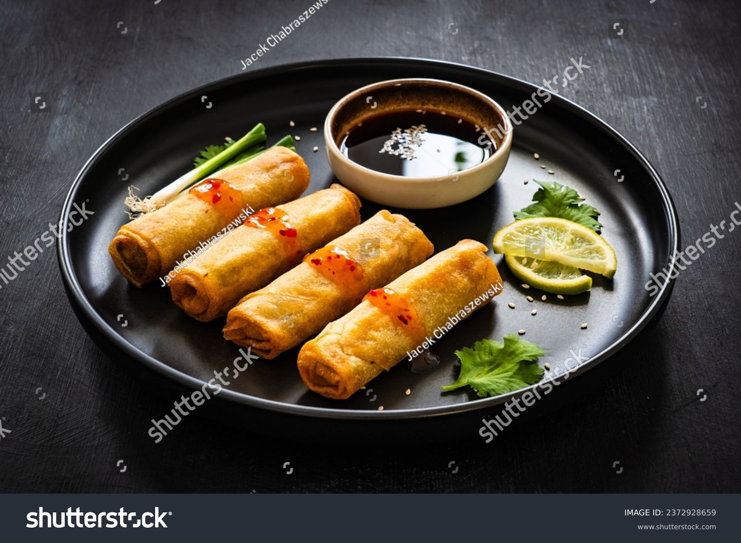 Vegetable filled spring rolls and soy sauce on black wooden table  #2372928659