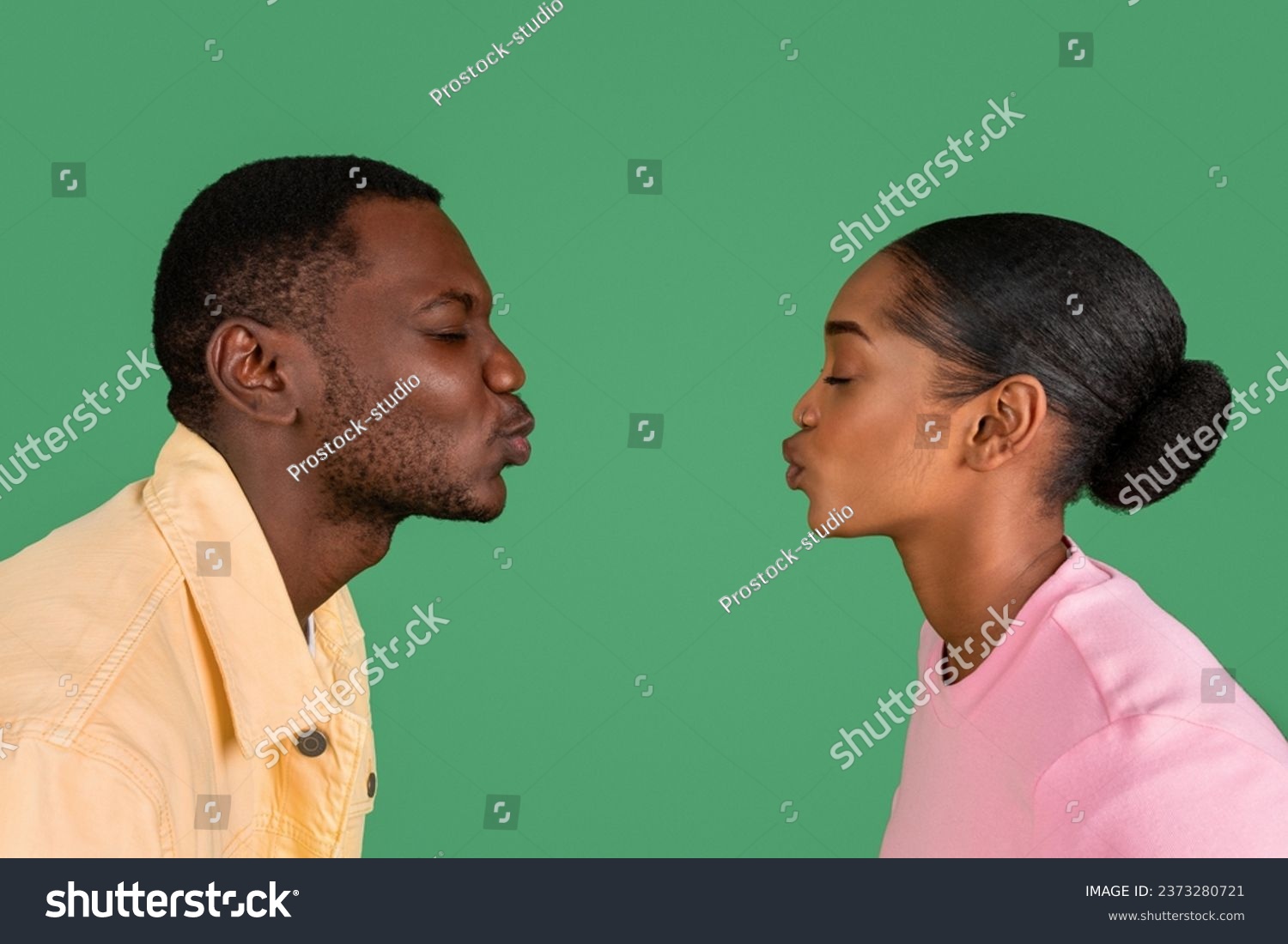 Side view of loving young black man and woman kissing with closed eyes, copy space between them, isolated on green studio background. Love, affection, bonding, relationships #2373280721