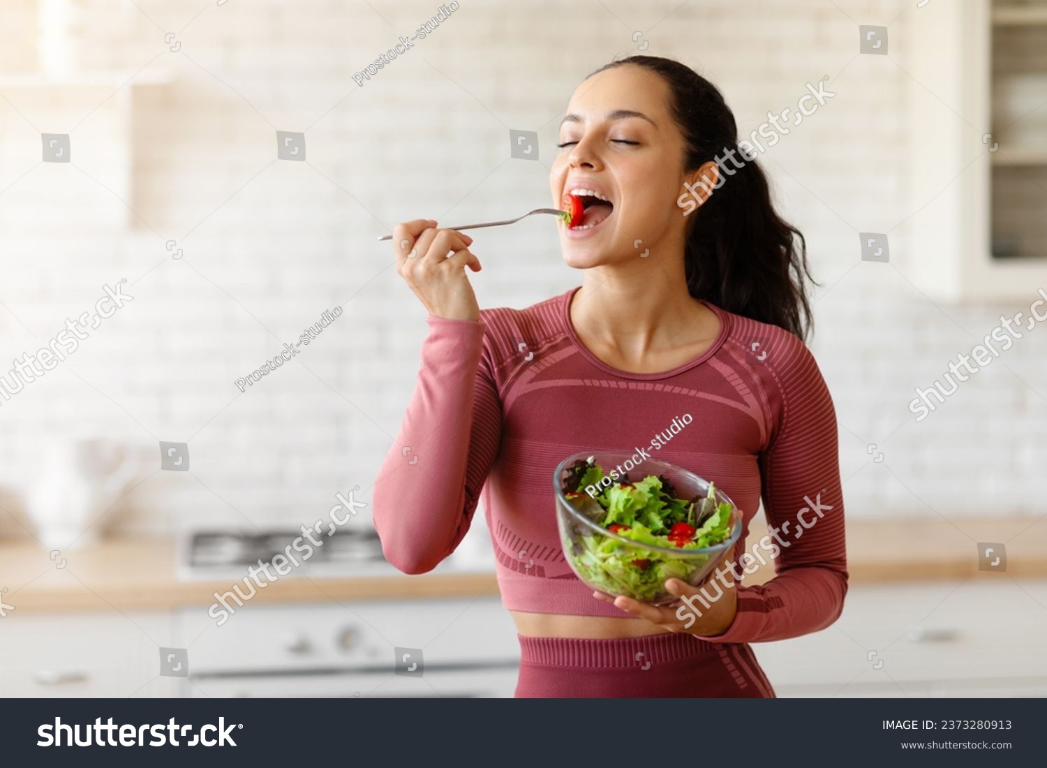 Weight Loss Diet. Happy sporty woman eats a big bowl of fresh salad in the kitchen indoor, slimming, advertising healthy living and nutrition. Easy meal for staying in shape #2373280913