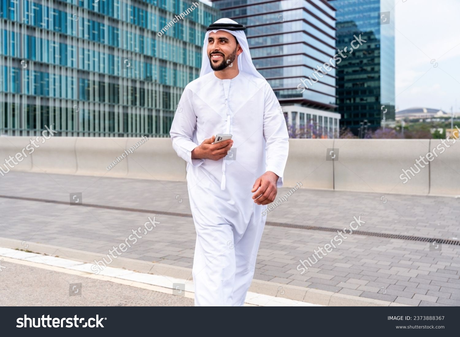 Arab middle-eastern man wearing emirati kandora traditional clothing in the city - Arabian muslim businessman strolling in urban business centre. #2373888367