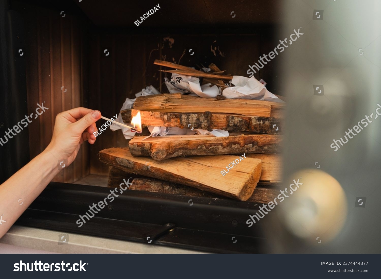 Female hand holds a matchstick, ready to ignite the firewood in a fireplace. #2374444377