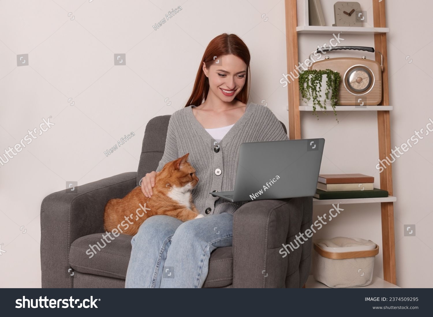 Happy woman with cat working in armchair at home #2374509295