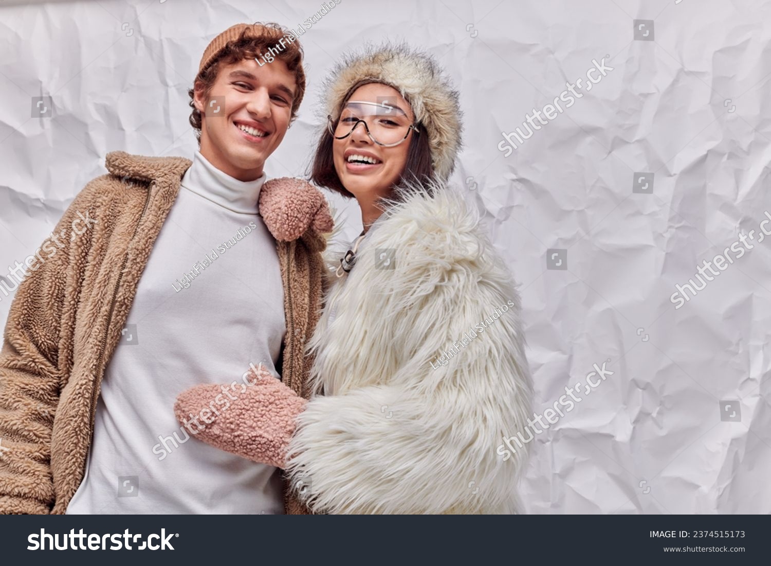 joyful interracial couple in fashionable warm outwear on white textured backdrop, winter fashion #2374515173