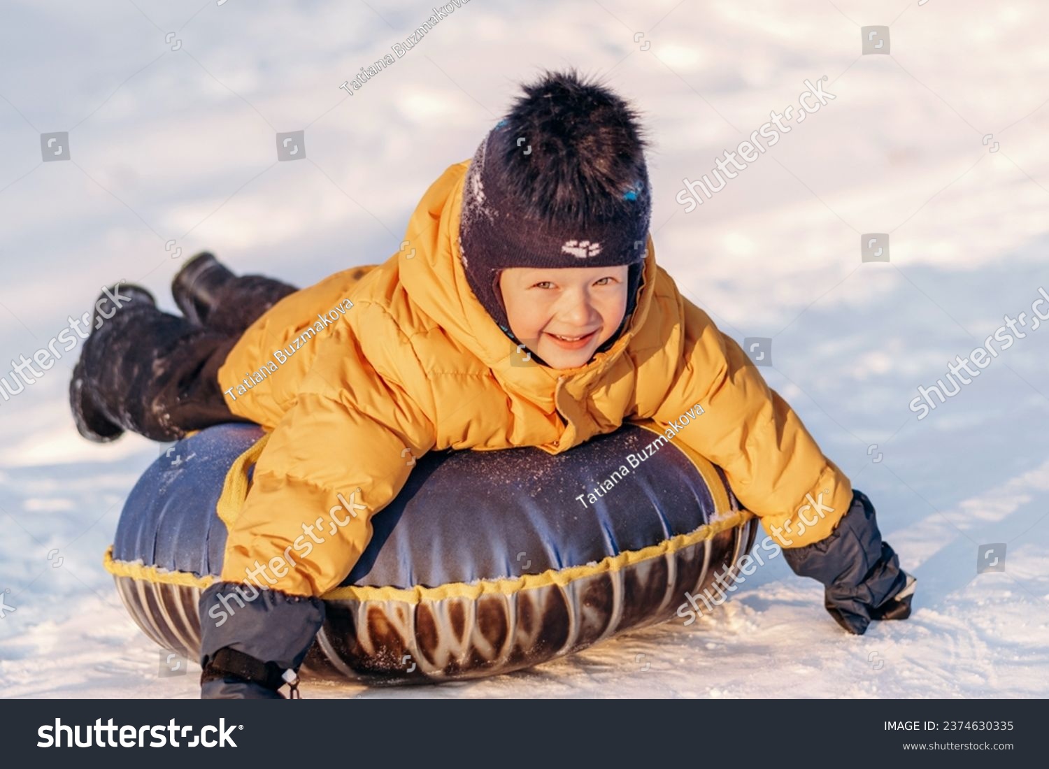 Active toddler boy in a yellow jacket sliding down the hill on snow tube.Winter fun,active lifestyle concept. #2374630335