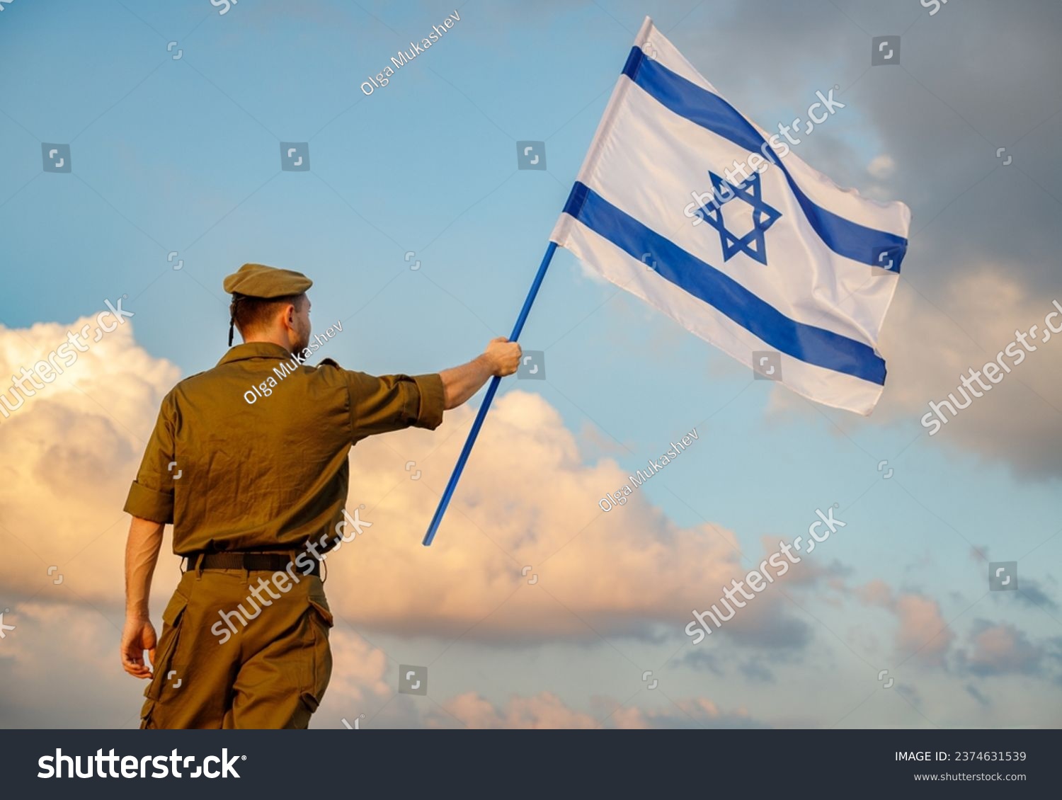 A guy in a soldier's uniform with an Israeli flag in his hand against a cloudy sky. Remembrance Day - Yom HaZikaron, Patriotic holiday, Israeli Independence Day - Yom Ha'atzmaut concept. #2374631539