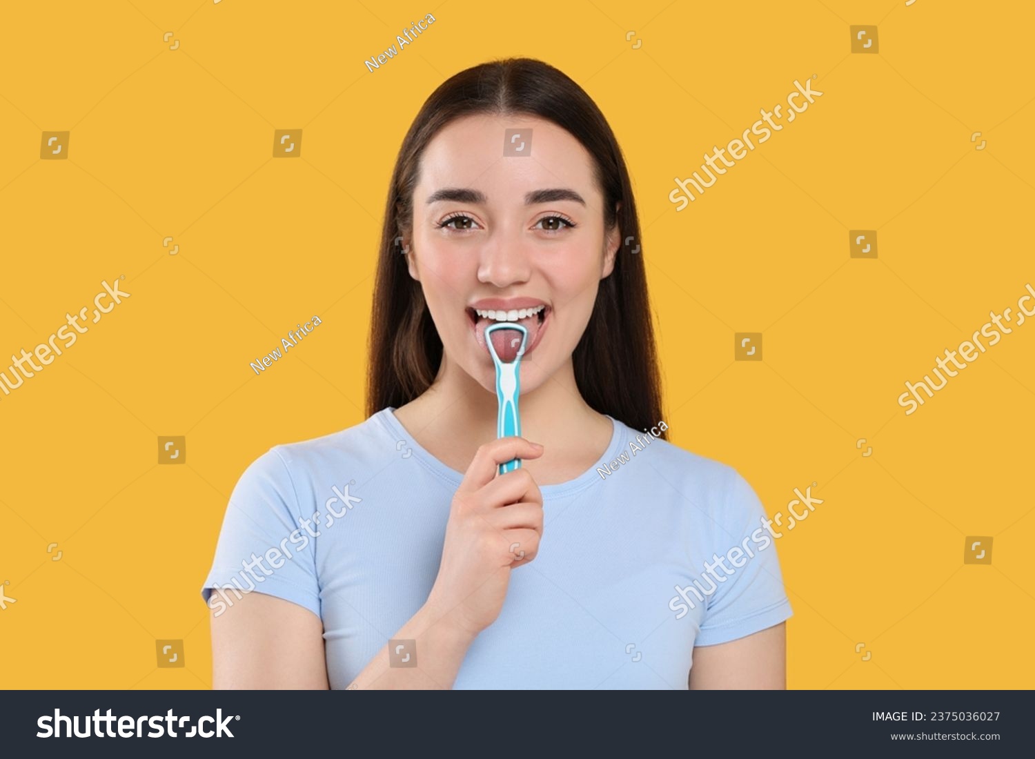 Happy woman brushing her tongue with cleaner on yellow background #2375036027