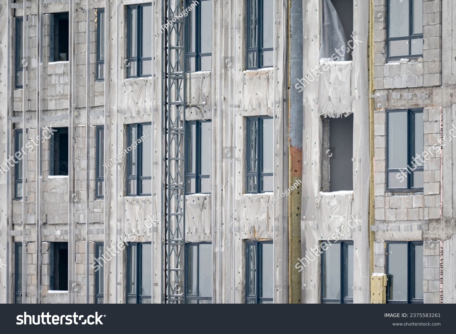 Construction of a new house. View of a fragment of an unfinished building made of gray concrete with multi-storey windows without glass. The concept of building and housing provision. #2375583261