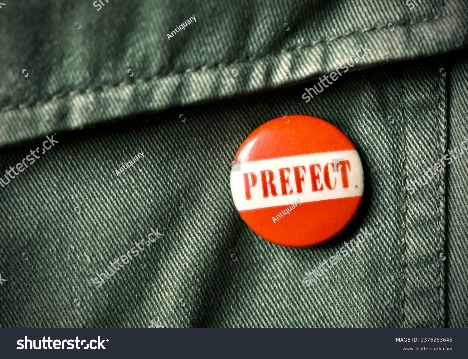 Vintage round school prefect tin pin button badge on green jacket taken in the United Kingdom October 2023 #2376283645