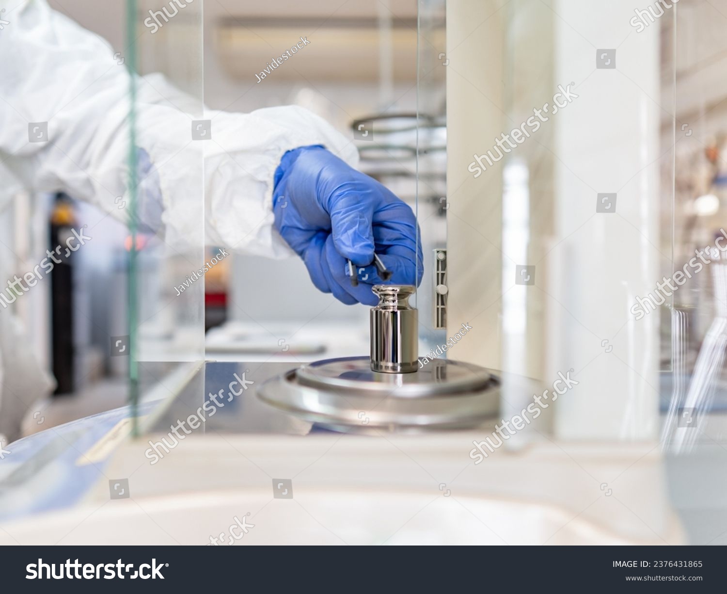 A operator's hand is holding steel calibration weight to place on the analytical balance. Concept of quality control in a laboratory. #2376431865