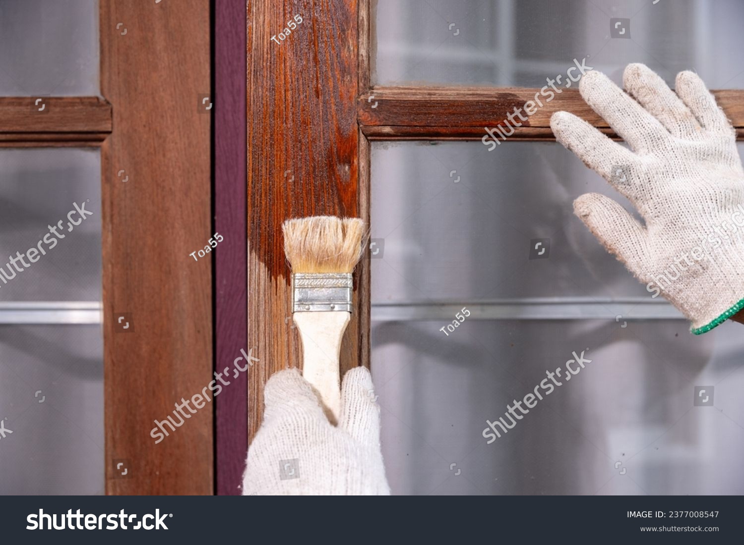 Worker use brush apply wood preserver after sandling the old surface of wooden window #2377008547