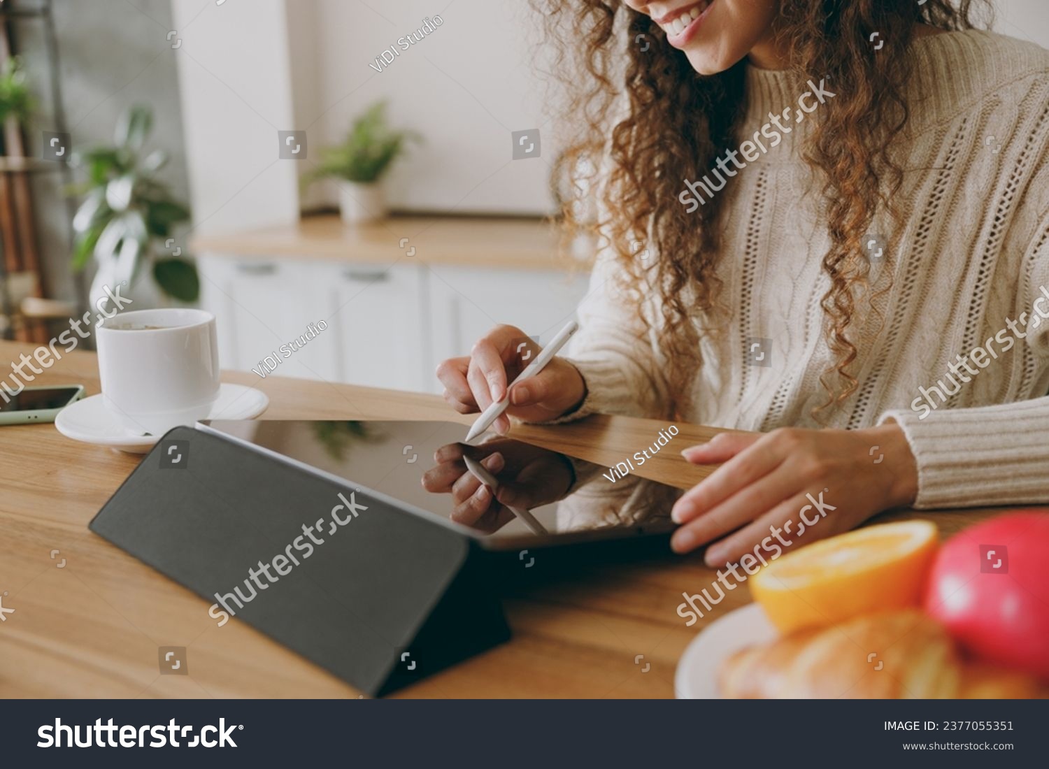 Cropped young graphic designer housewife woman wears casual clothes sweater hold in hand work use write draw stylus pc pen sit at table in light kitchen at home alone. Lifestyle cooking food concept #2377055351