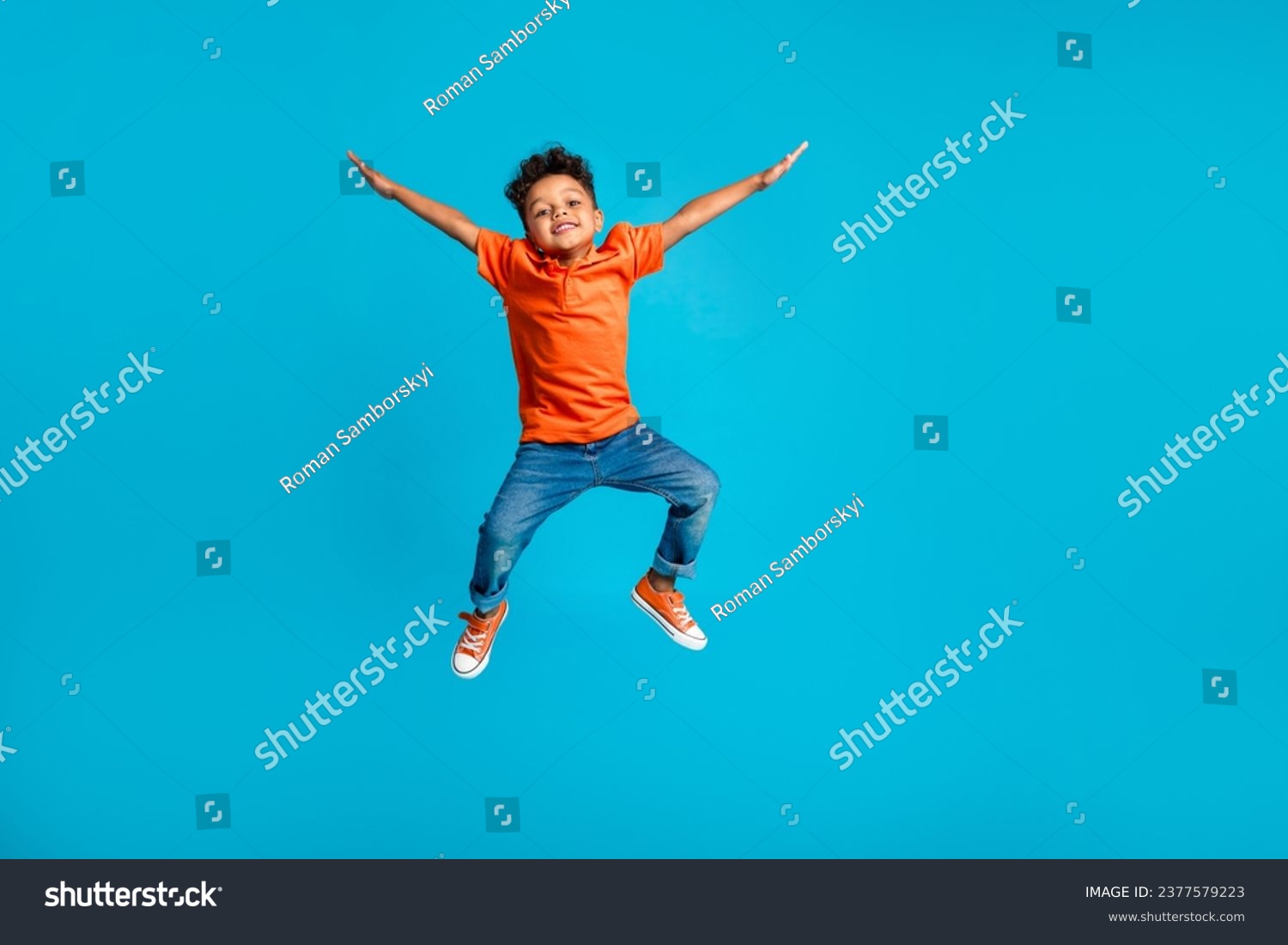Full body cadre of jumping energetic latin small kindergarten age boy hands up positive star symbol hands isolated on blue color background #2377579223
