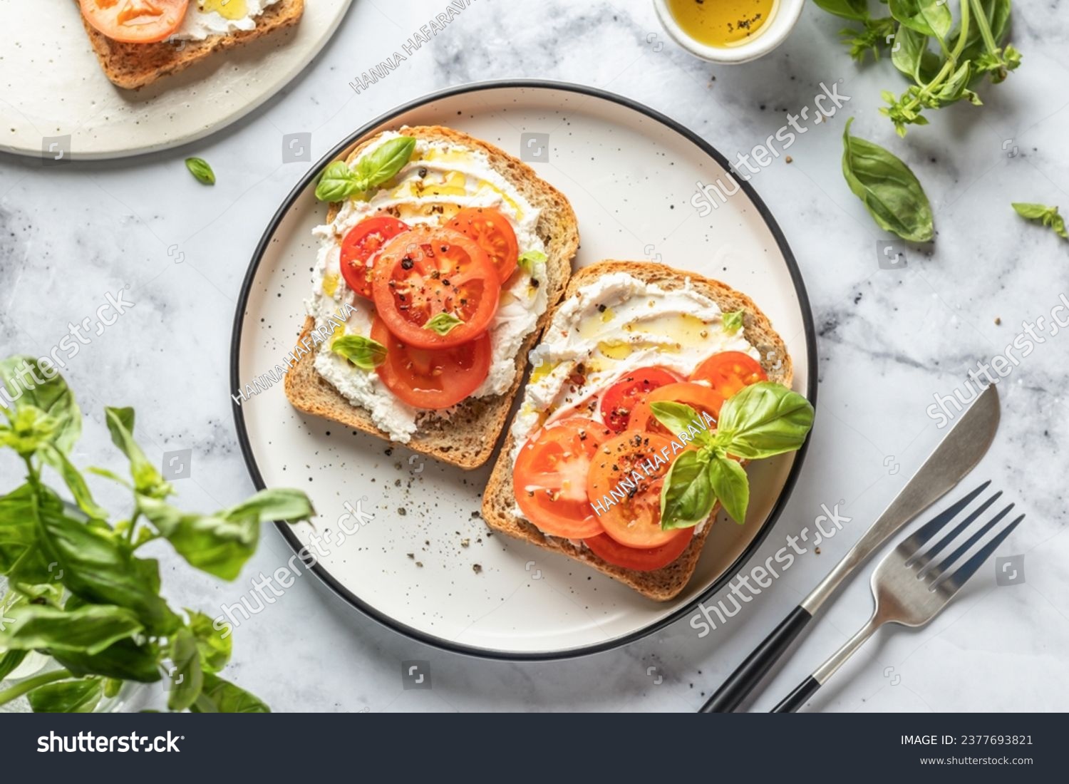 Sandwiches or toasts with tomatoes, cream cheese, olive oil and basil on a plate on white marble background. Traditional italian mediterranean food. Horizontal, top view, flat lay #2377693821