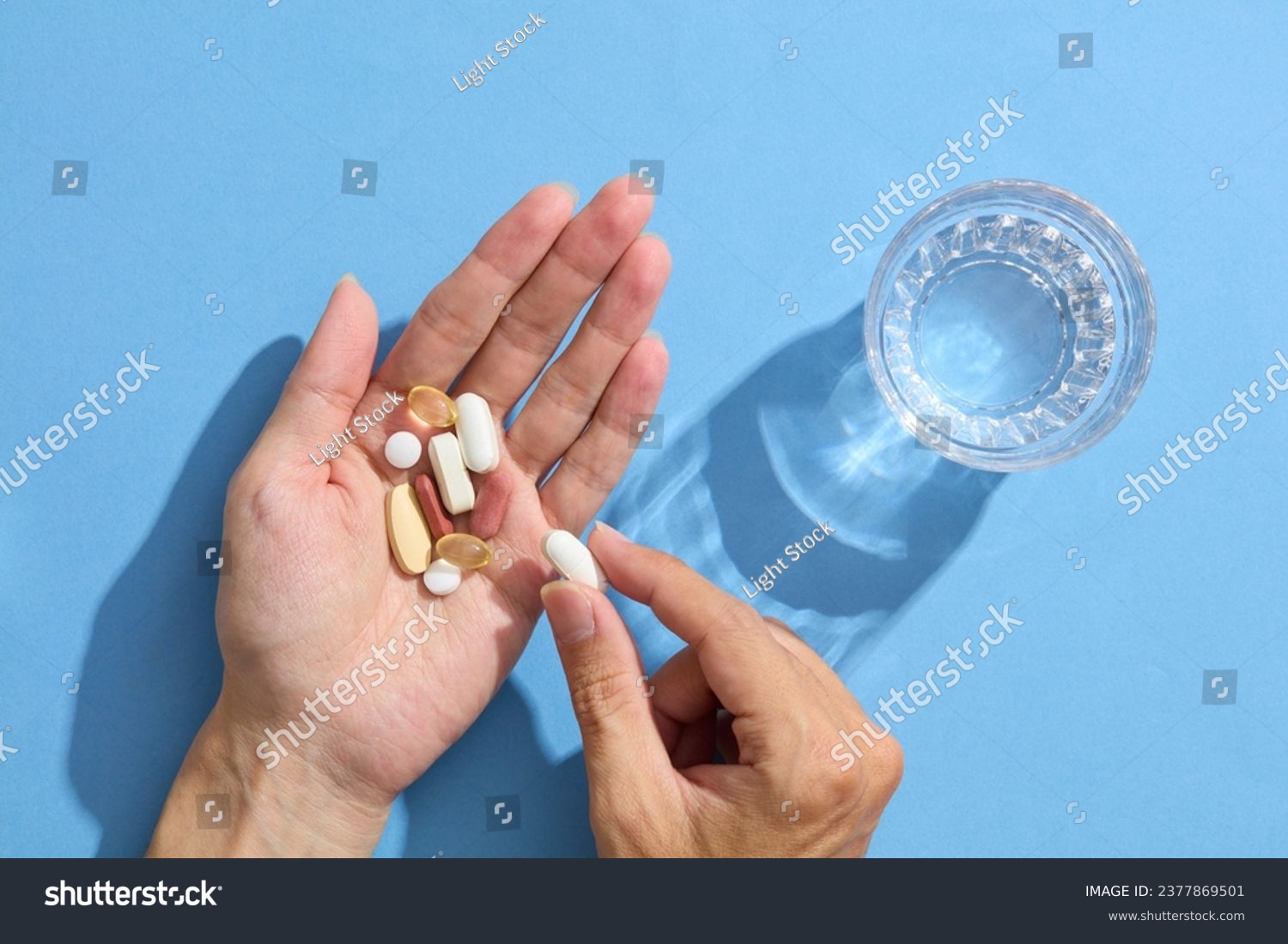 Close up of a woman's hand holding multiple pills with a glass of water. Taking medication for headache relief, pain management, drinking water from the glass. The concept of healthcare, medicine. #2377869501