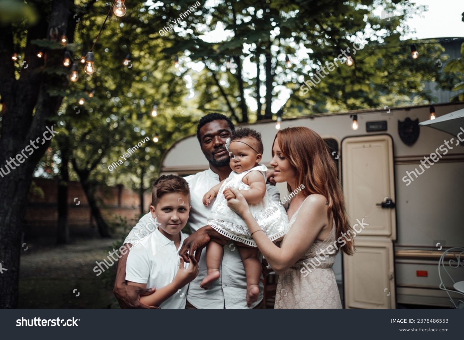 Mixed race family with white son and infant swarthy daughter spend time together in camper park outdoor. African american man with his fair skinned wife and kids enjoying summer vacation in open air #2378486553