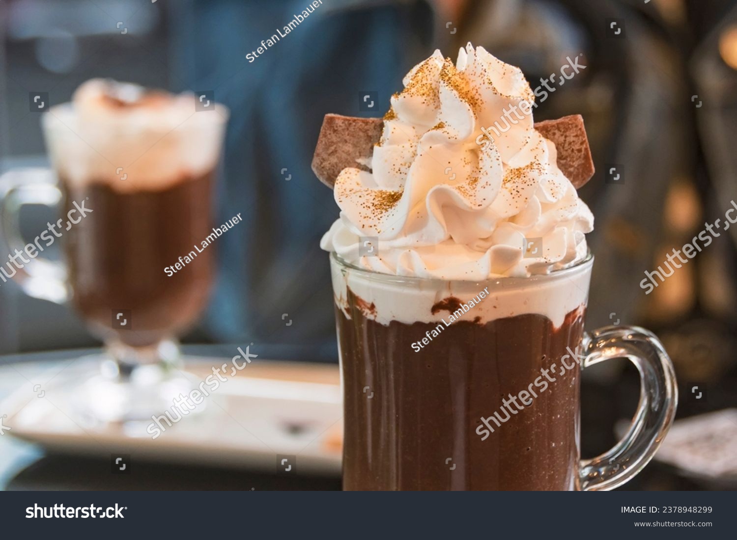 Hot chocolate with whipped cream and golden edible glitter in a transparent cup. Blurred background. #2378948299