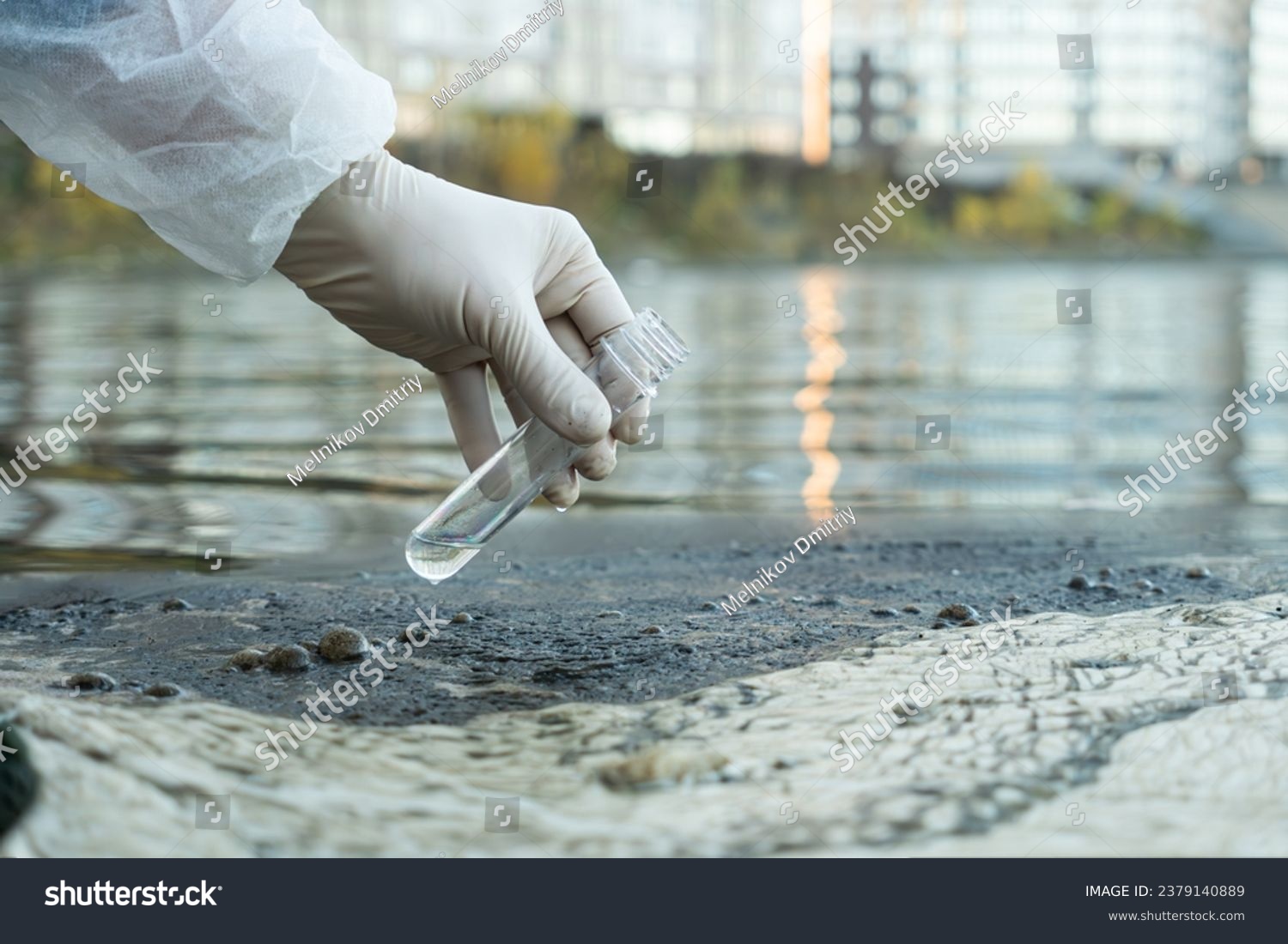 female ecologist in a protective glove holding a test tube with water from a city river #2379140889