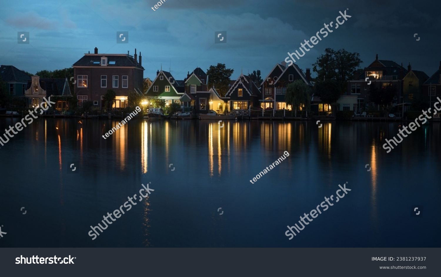 Night shot of houses in Dutch village on riverbank. Lights reflecting on water surface #2381237937