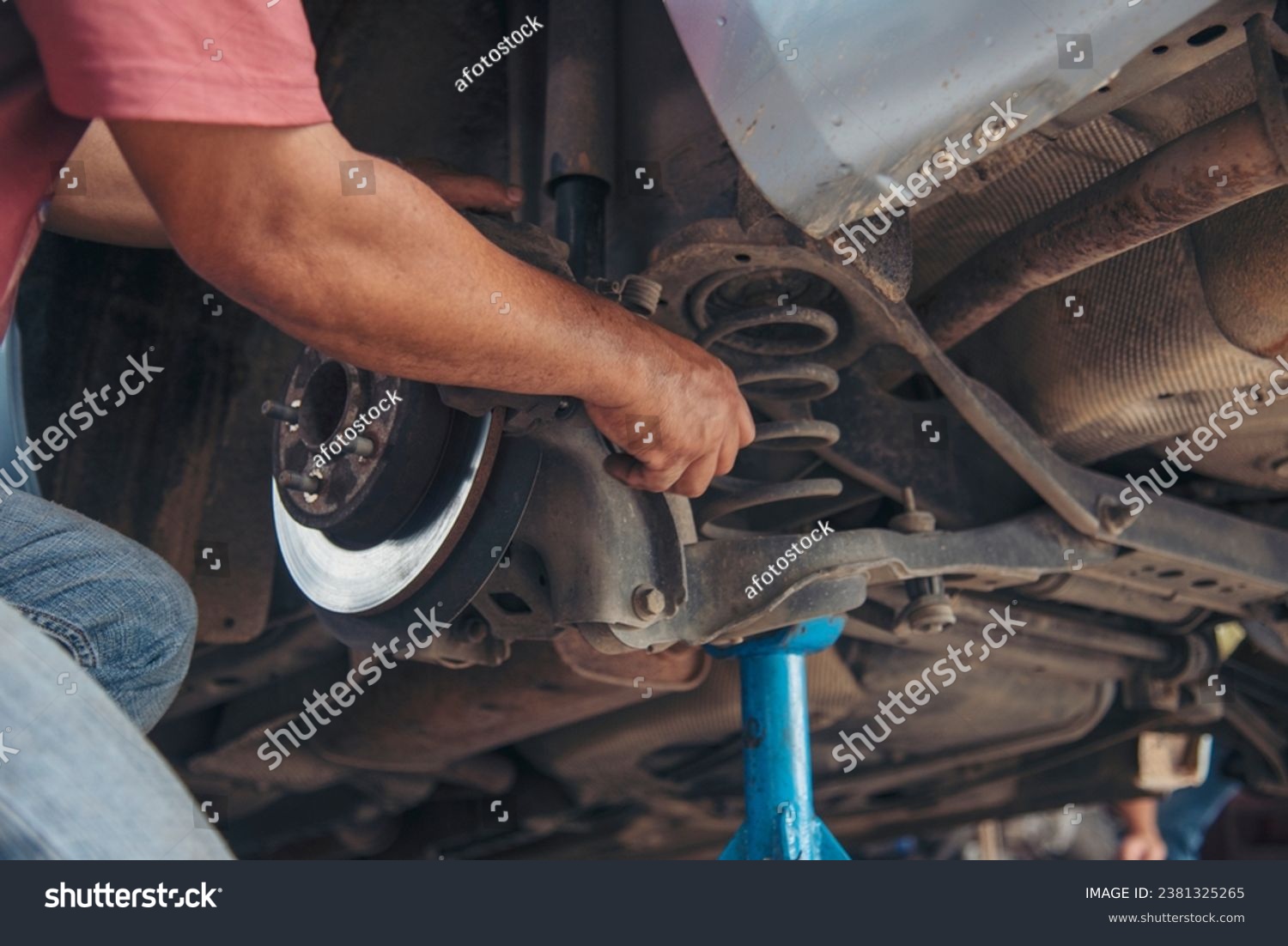 Close up Mechanic man hands repairing car auto repair shop uses jack change tyre. Man hands fixing Shock absorber machinery vehicle mechanical service. Vehicle Car overhaul maintenance engineer #2381325265