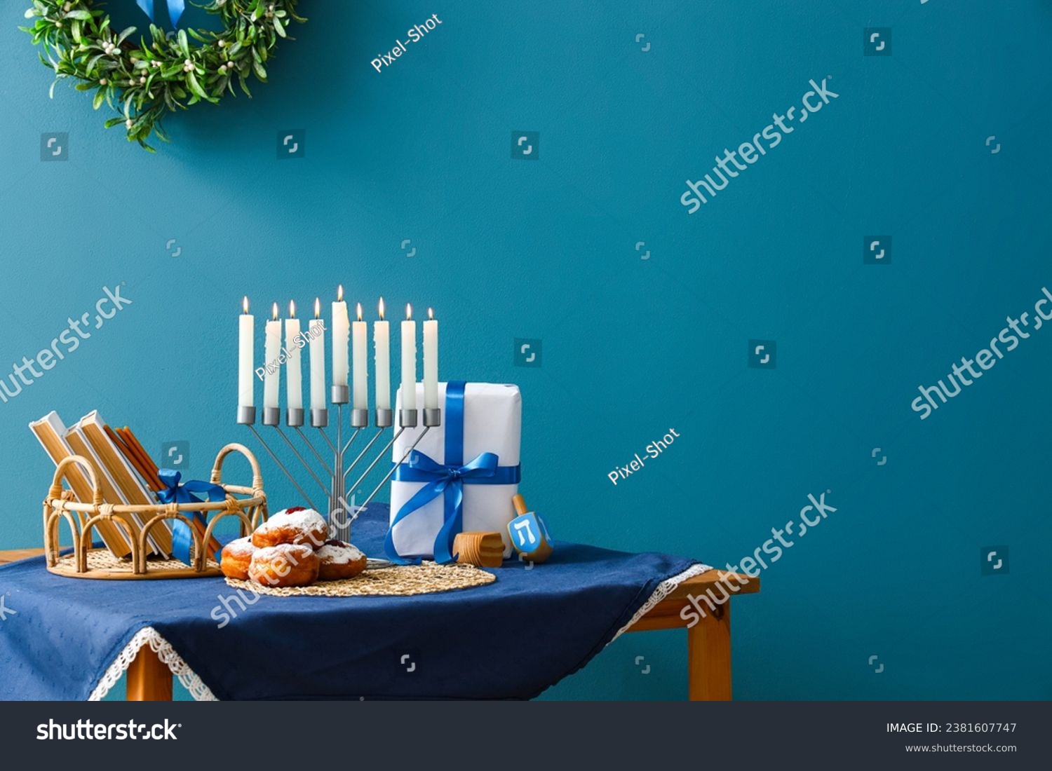 Menorah with donuts, books, dreidels and gift for Hannukah on table near blue wall #2381607747