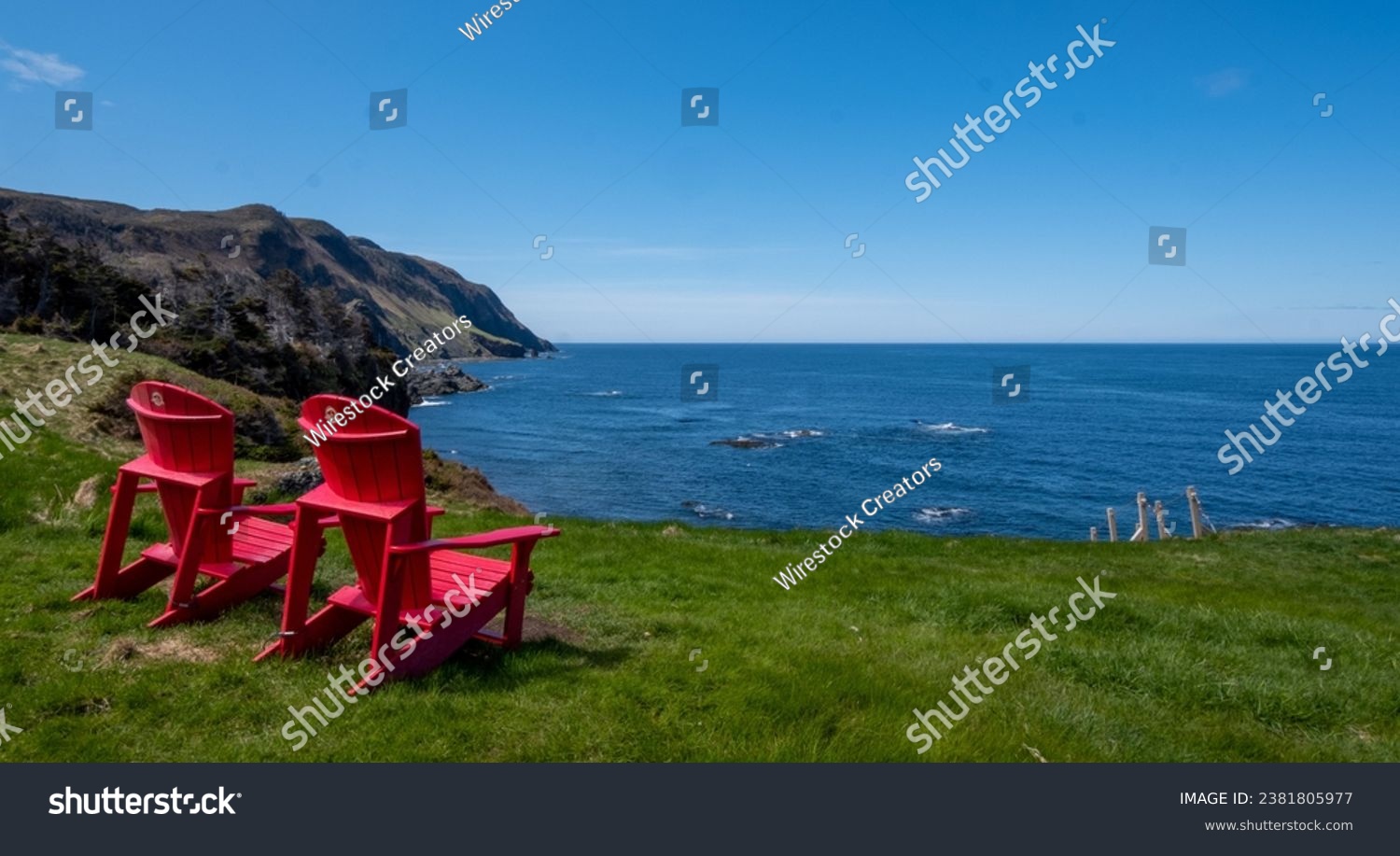 Two red empty chairs on lush green grass on the seashore in Newfoundland, Canada #2381805977
