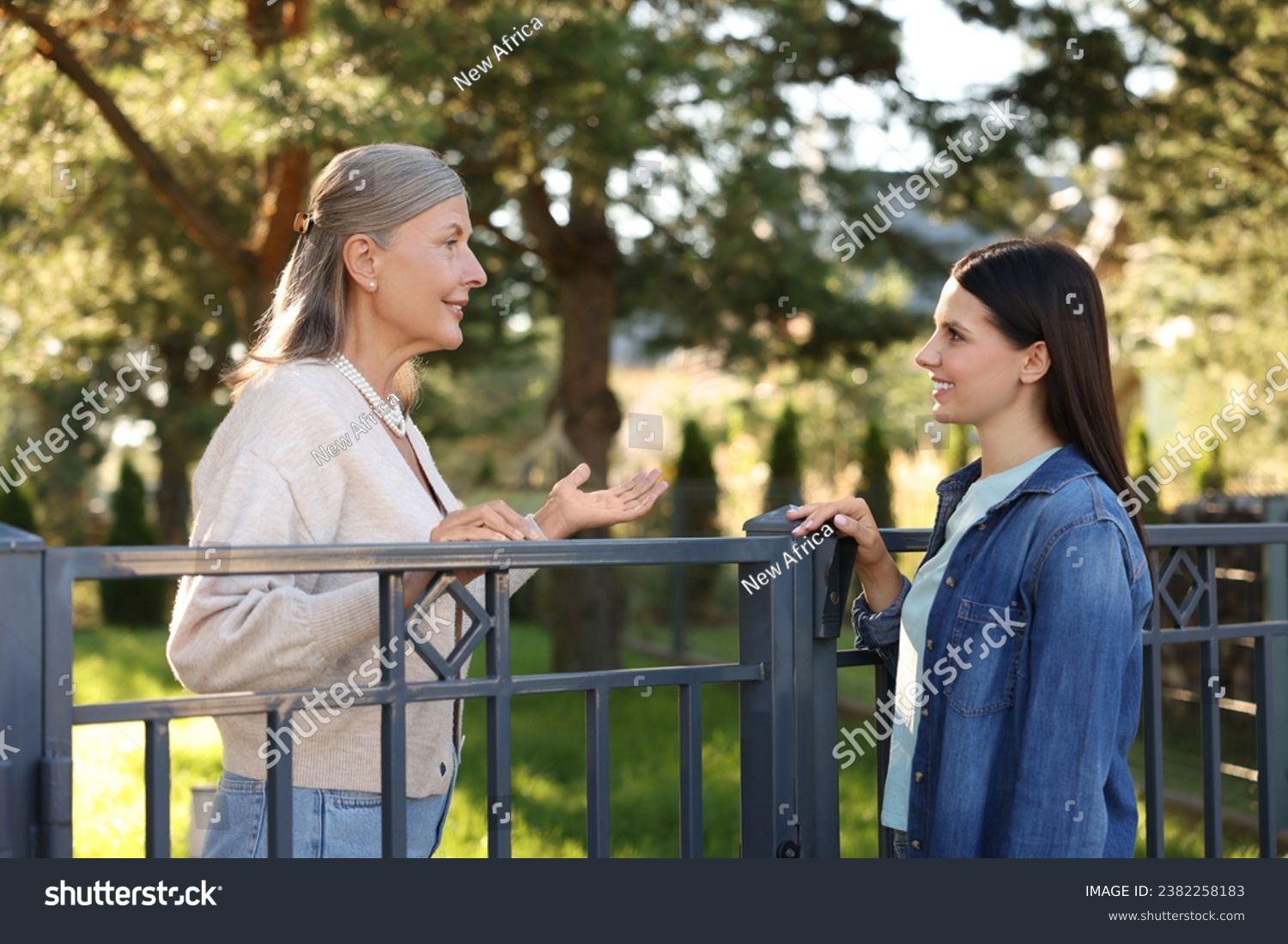 Friendly relationship with neighbours. Happy women talking near fence outdoors #2382258183