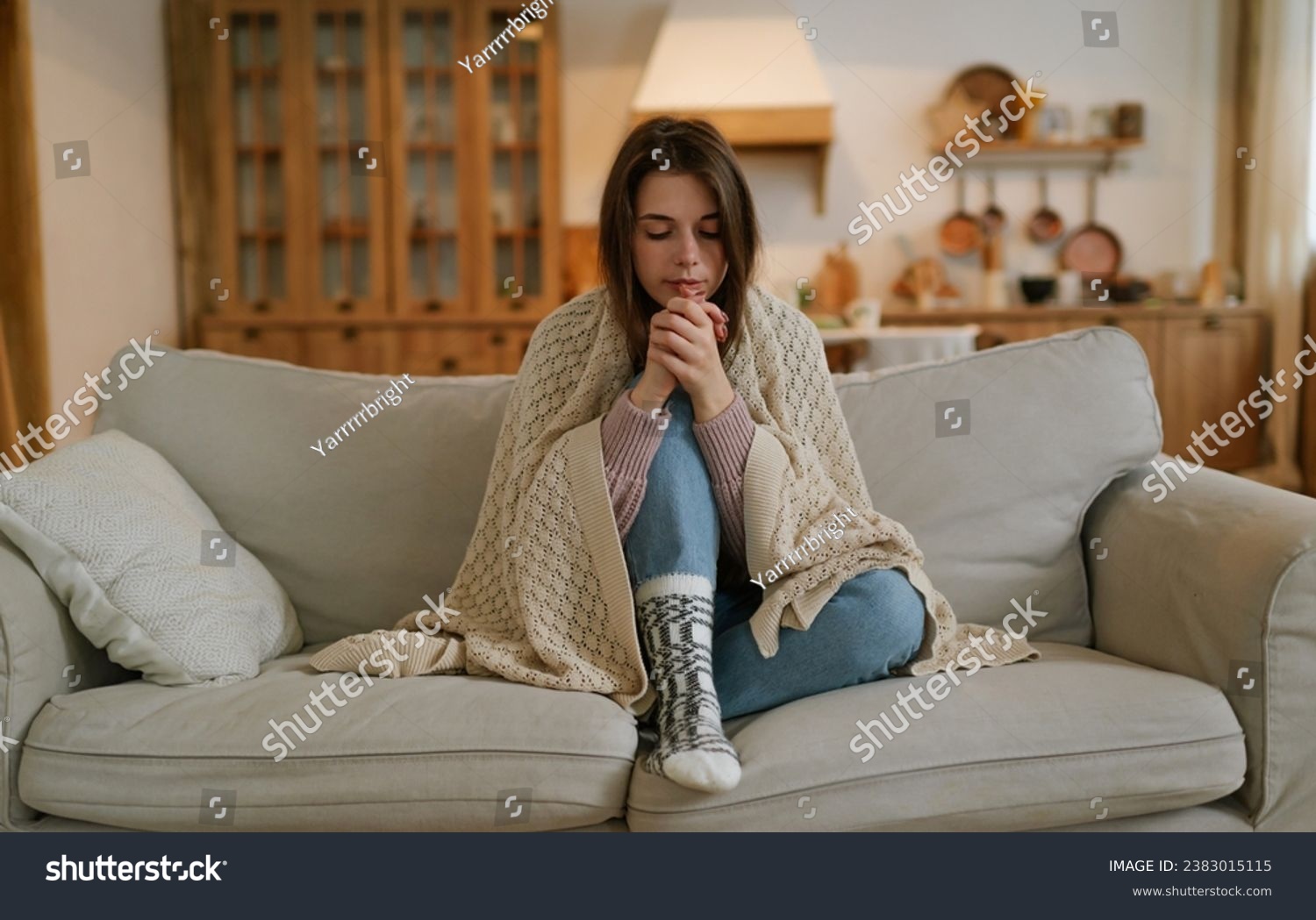 A woman freezes in winter. A young girl in warm woolen socks and wrapped in a blanket tries to keep warm while sitting on the sofa at home. Keep warm. #2383015115
