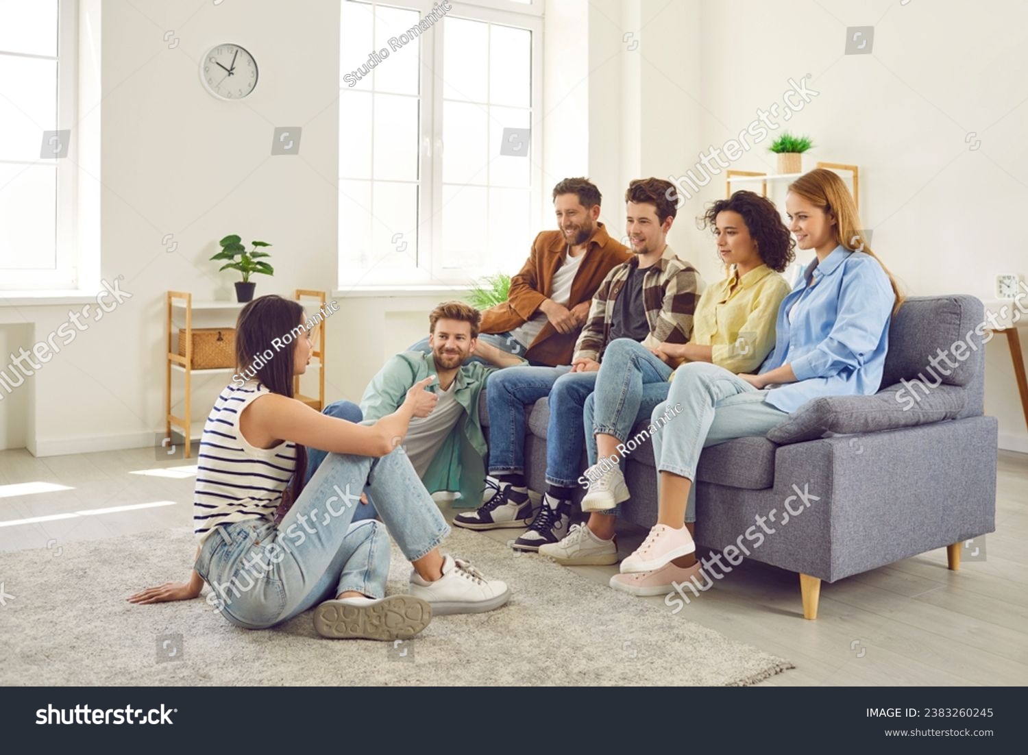 Group of friends hanging out together. Several young people meeting at somebody's place. Young men and women sitting on sofa and listening to girl who is sitting on floor and talking about something #2383260245