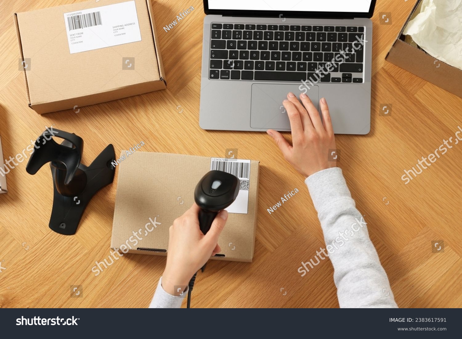 Woman with scanner reading parcel barcode at wooden table, top view. Online store #2383617591