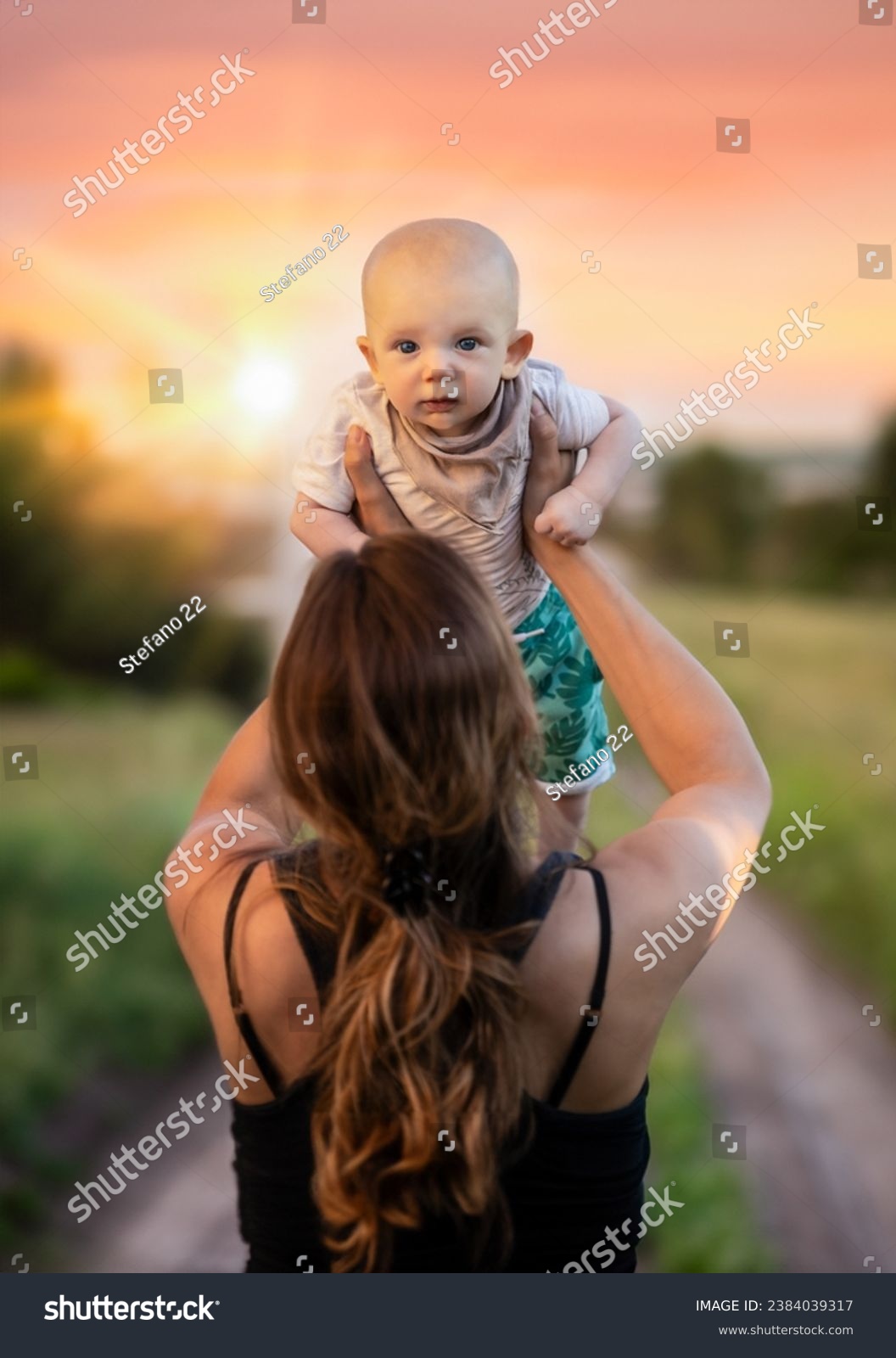 Sunset with a woman holding a small boy above her head. #2384039317