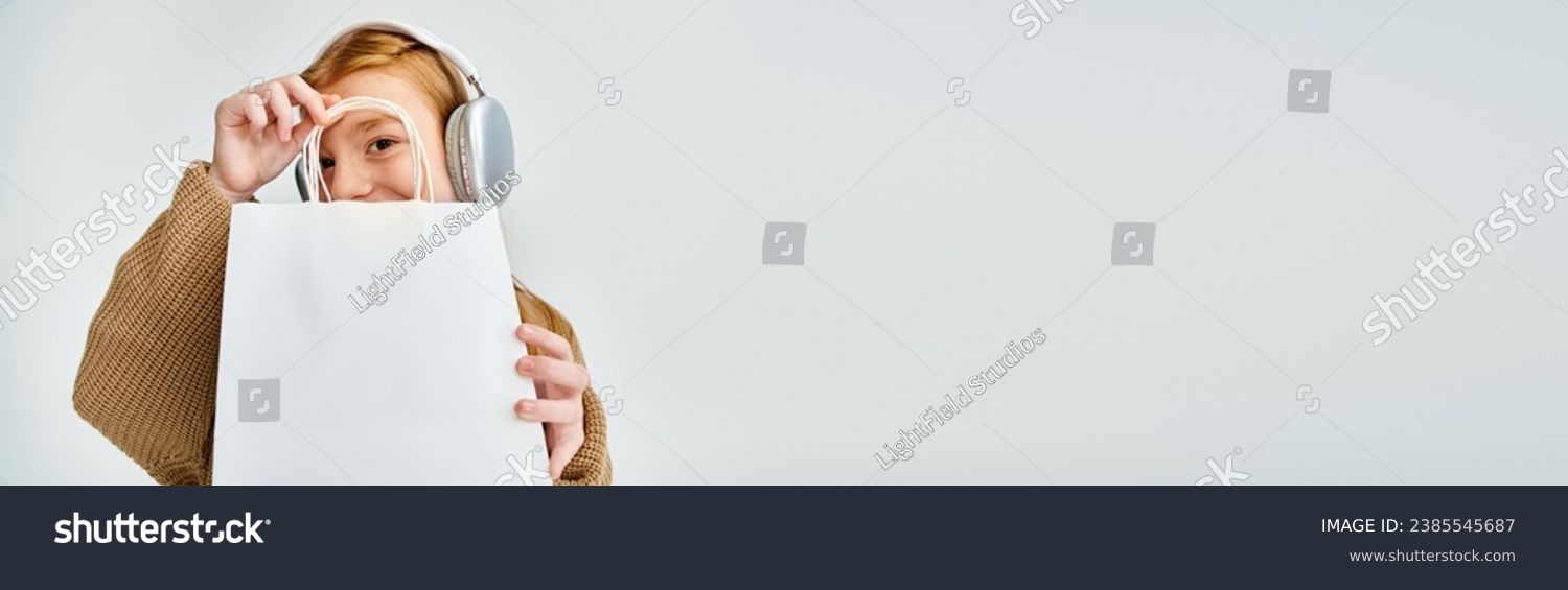 jolly little girl with headset and present bag in front of her face, fashion concept, banner #2385545687