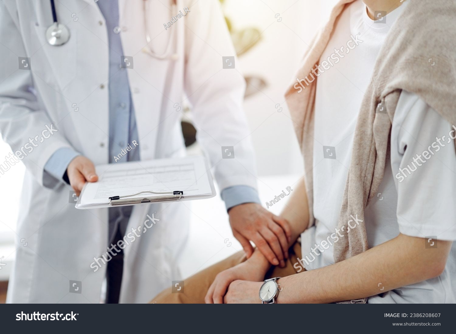 Doctor and patient in clinic. Friendly physician examining a young woman with a one hand while keeping a clipboard with medical records in another. Medicine concept #2386208607