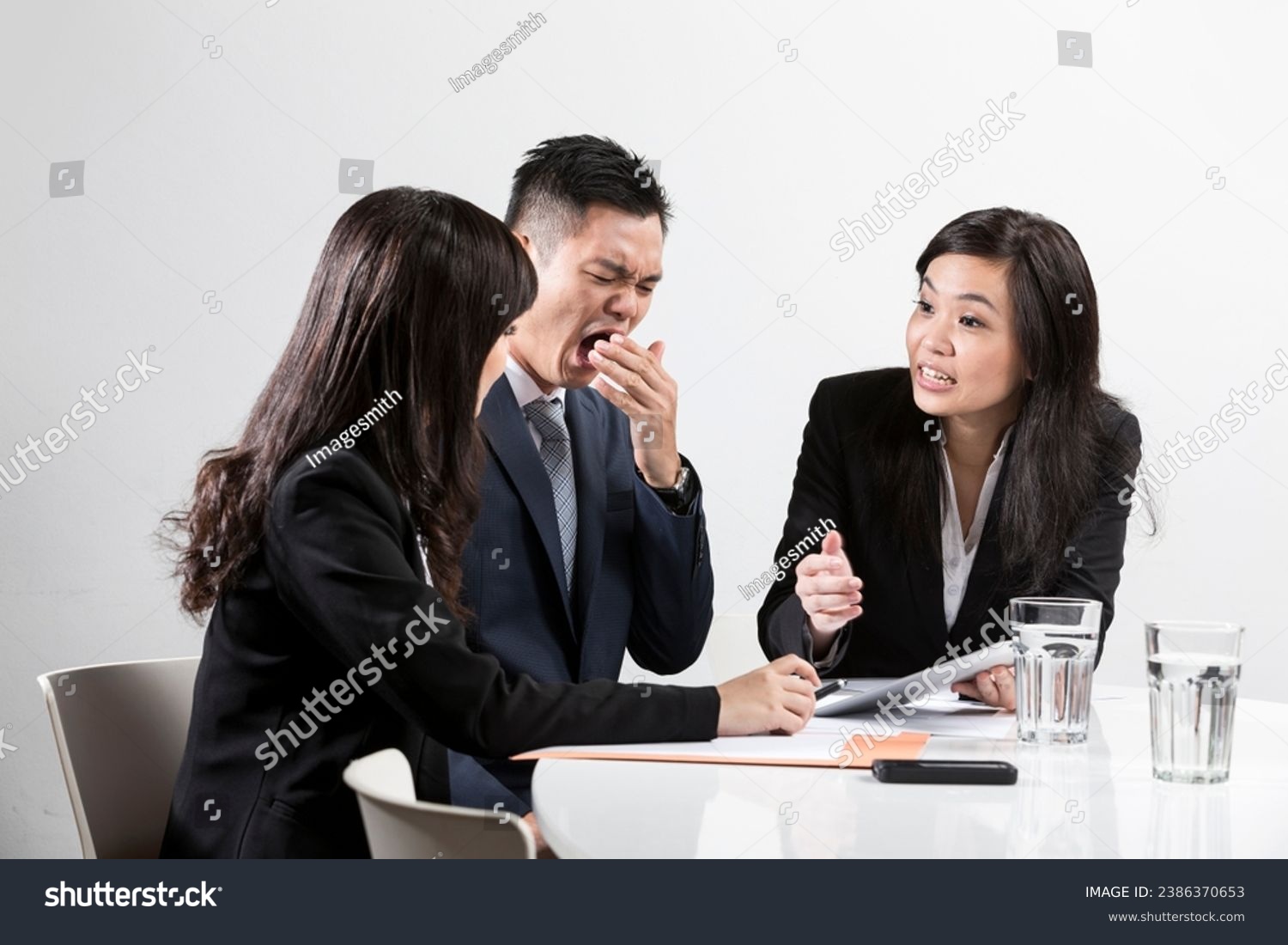 Chinese business man yawning during a business meeting in front of work colleges  #2386370653