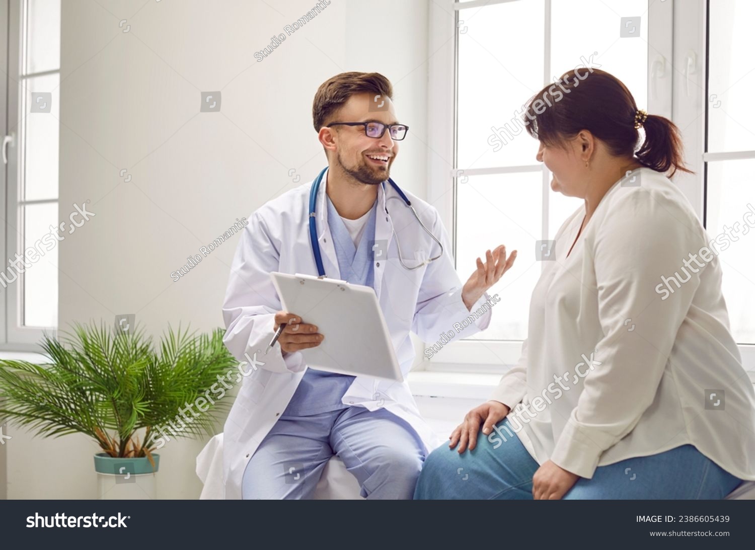 Portrait of fat overweight female patient in medical office listening to a friendly doctor holding report file with appointment and giving consultation a woman during medical examination in clinic. #2386605439