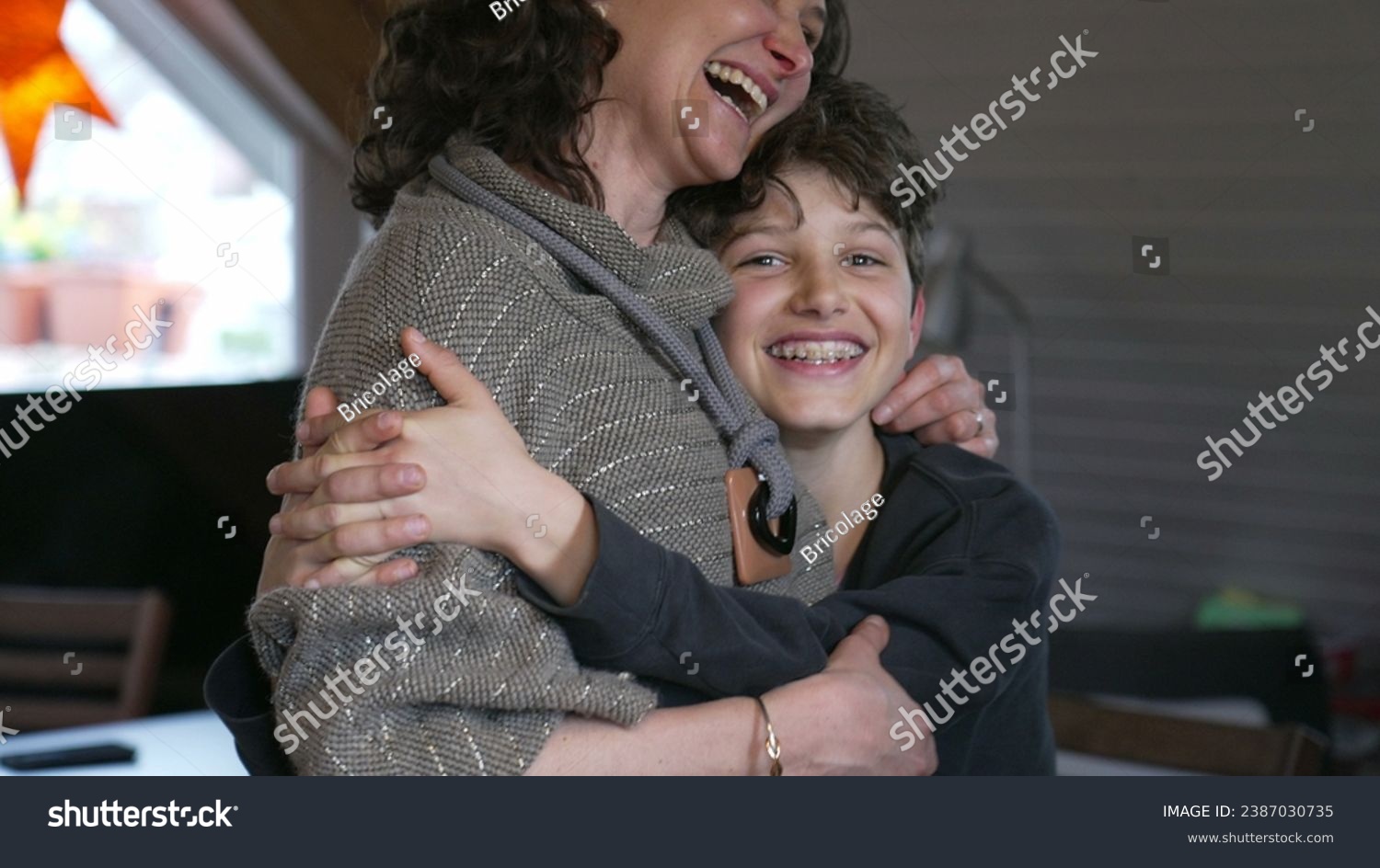 Candid mother and pre-teen boy laughing together. Authentic moment of family lifestyle joy with child with arm around mom in affectionate embrace #2387030735
