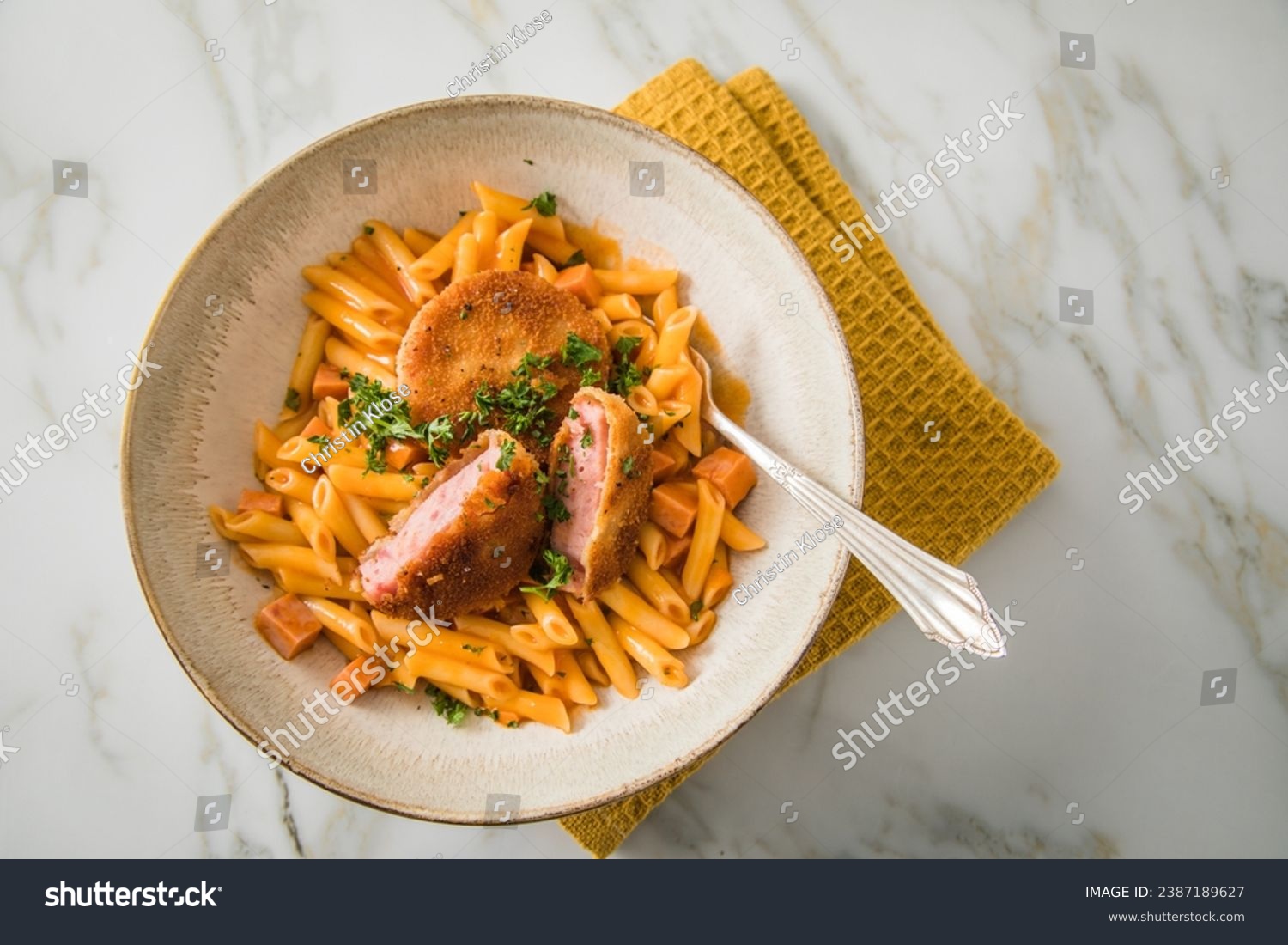 Jägerschnitzel escalope chasseur a East German DDR GDR specialty of breaded fried sausage slice, tomato sauce, Macaroni Penne pasta, parsley in bowl, cutlery, napkin, marble background #2387189627