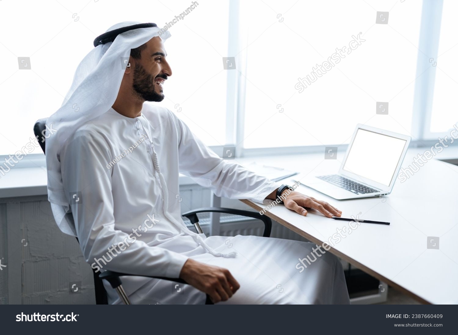 Handsome man with dish dasha working in his business office of Dubai. Portraits of a successful businessman in traditional emirates white dress. Concept about middle eastern cultures. #2387660409
