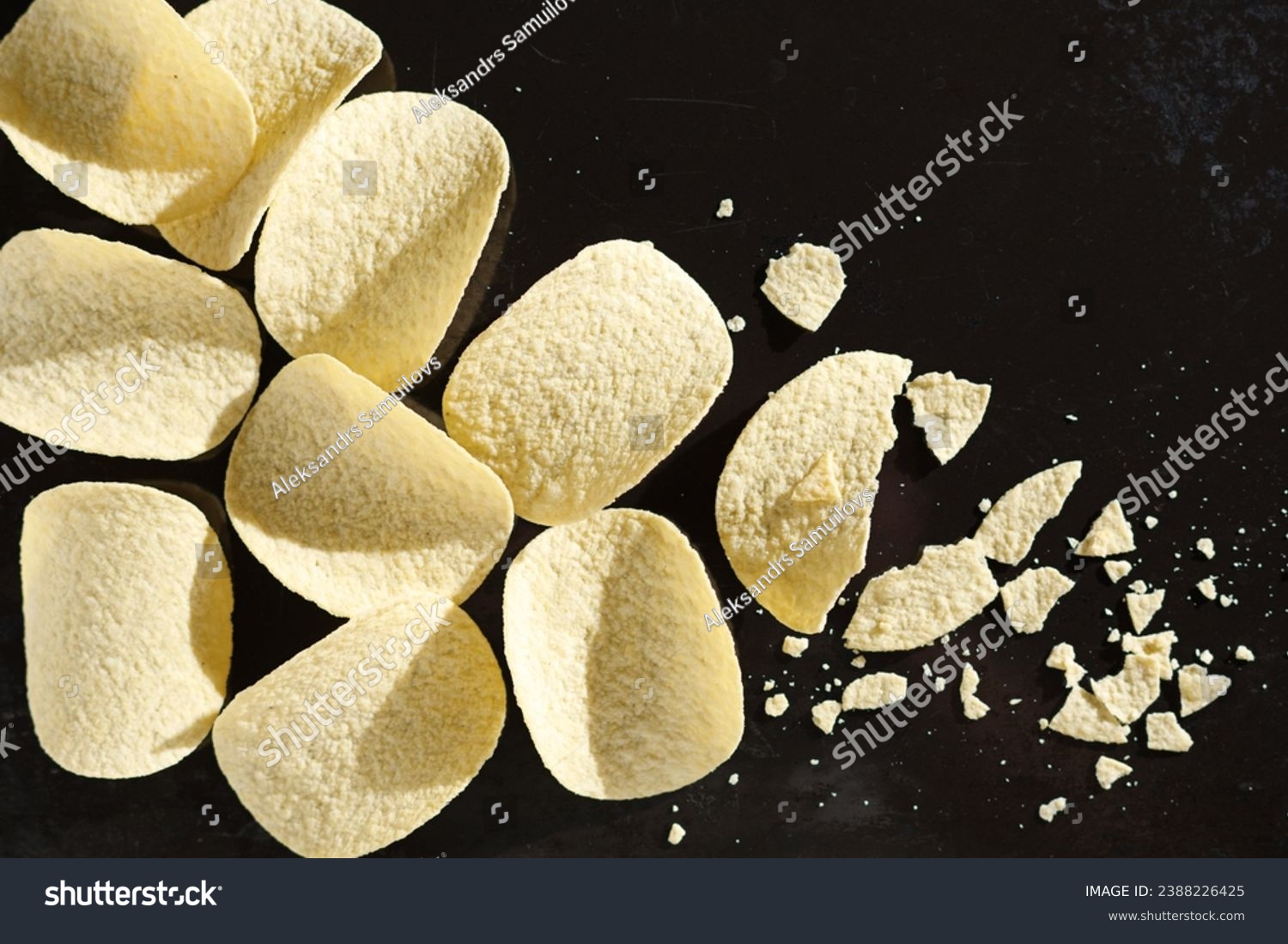 Tasty potato chips whole end broken on a black tray background, top view. Good snack for beer #2388226425