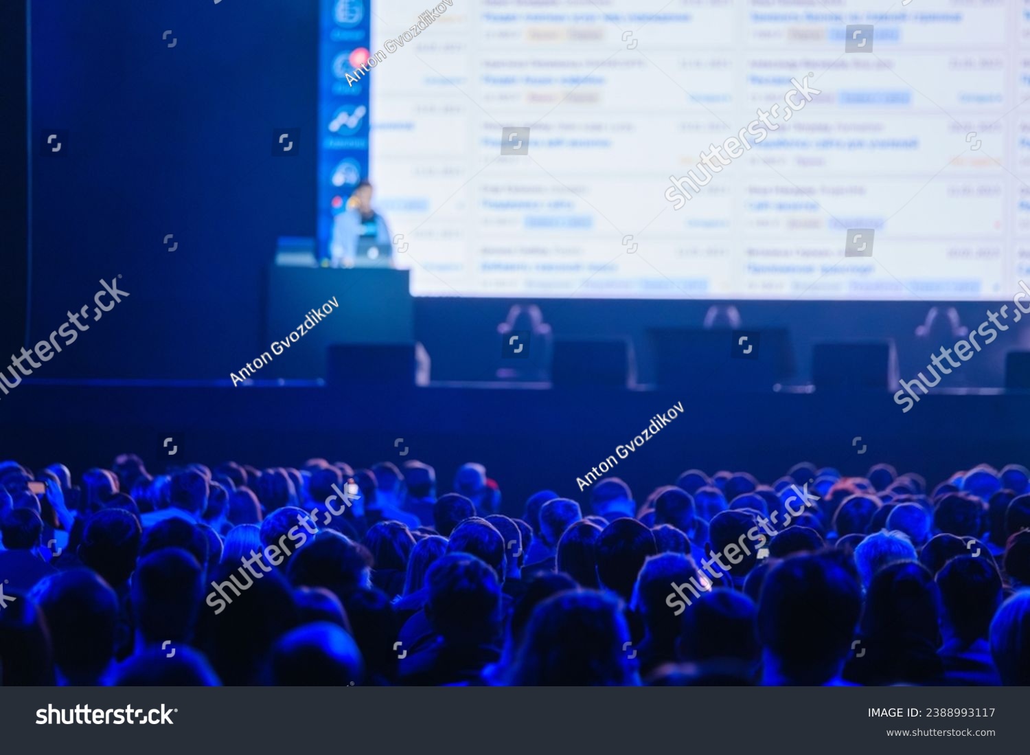 Back view of business crowd attending global presentation in illuminated blue auditorium #2388993117