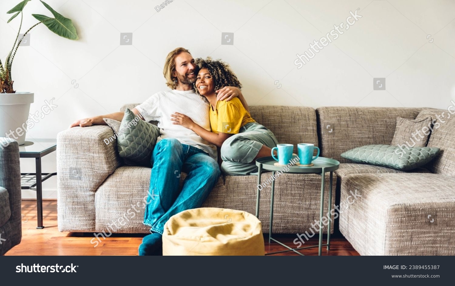Cheerful multiracial couple sitting on sofa in the living room - Happy family moving in new home - Real estate and stylish furniture concept #2389455387