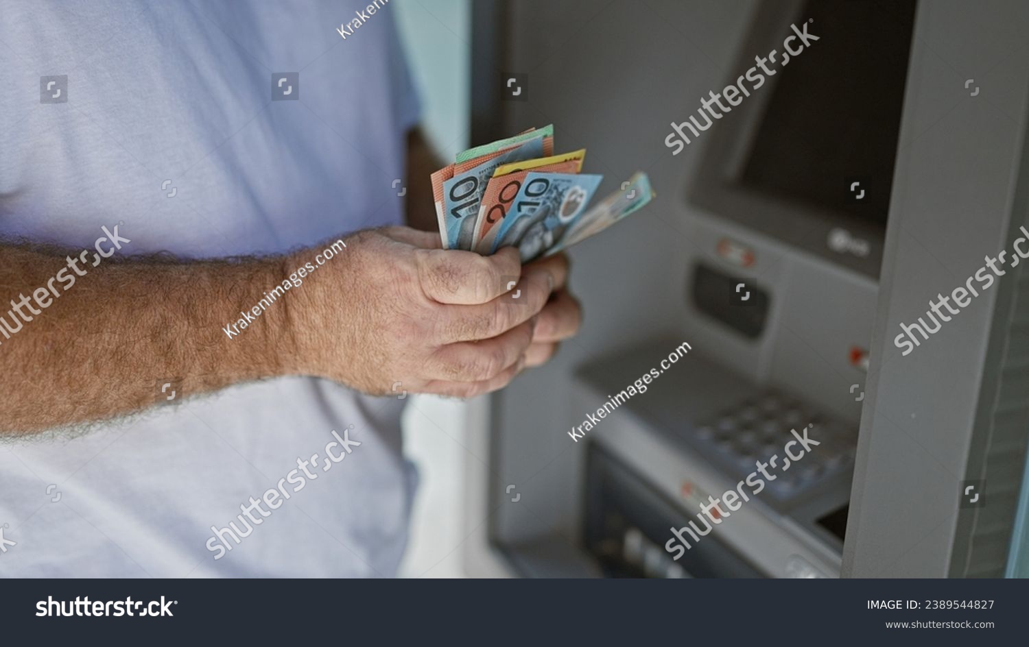 Handsome middle-aged caucasian man outside on urban street, captivating portrait of him holding wallet counting australian cash dollars at atm machine, engaging in banking transaction. #2389544827