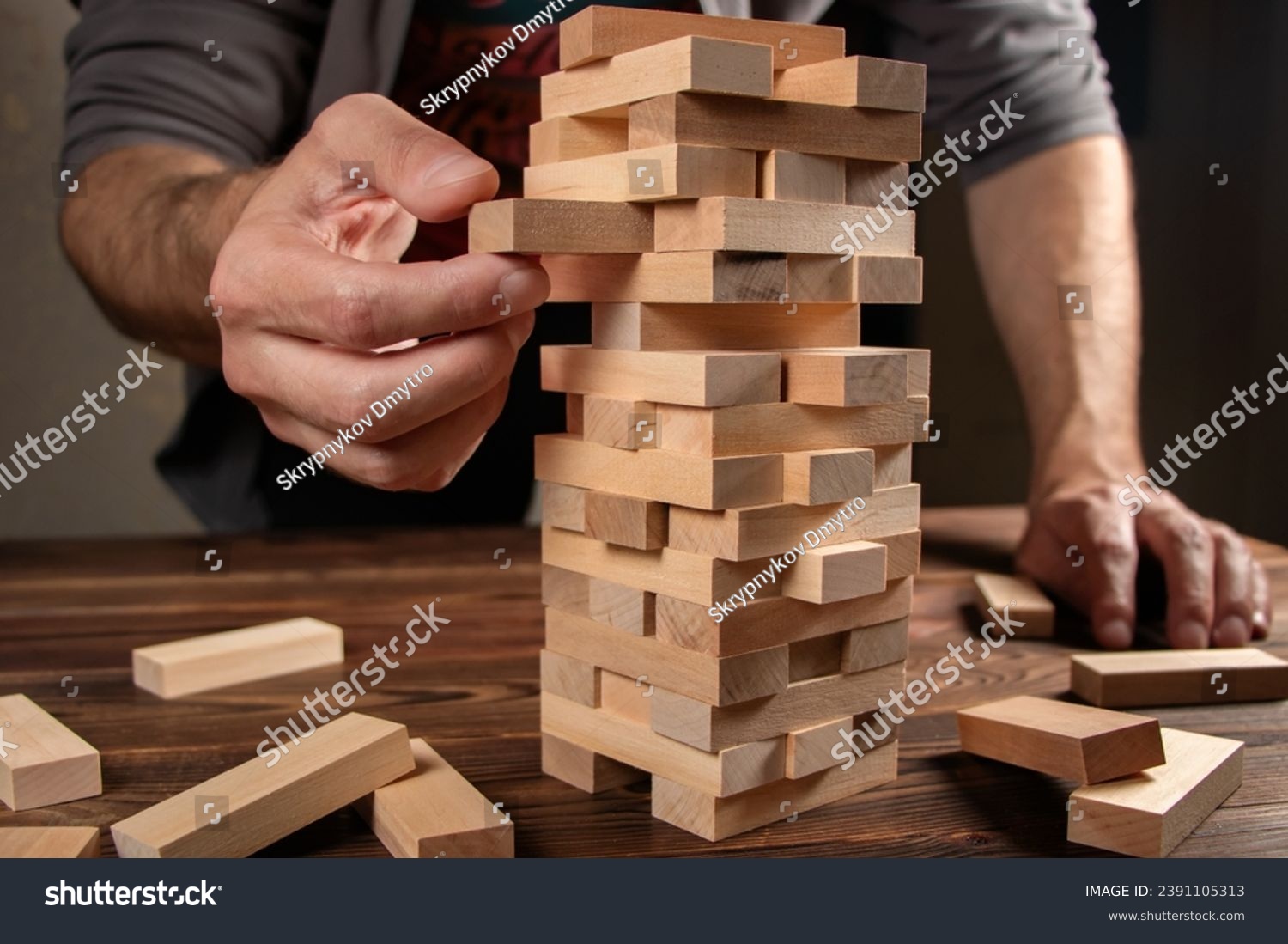 Hand of engineer playing a blocks wood tower game jenga on blueprint or architectural project. #2391105313