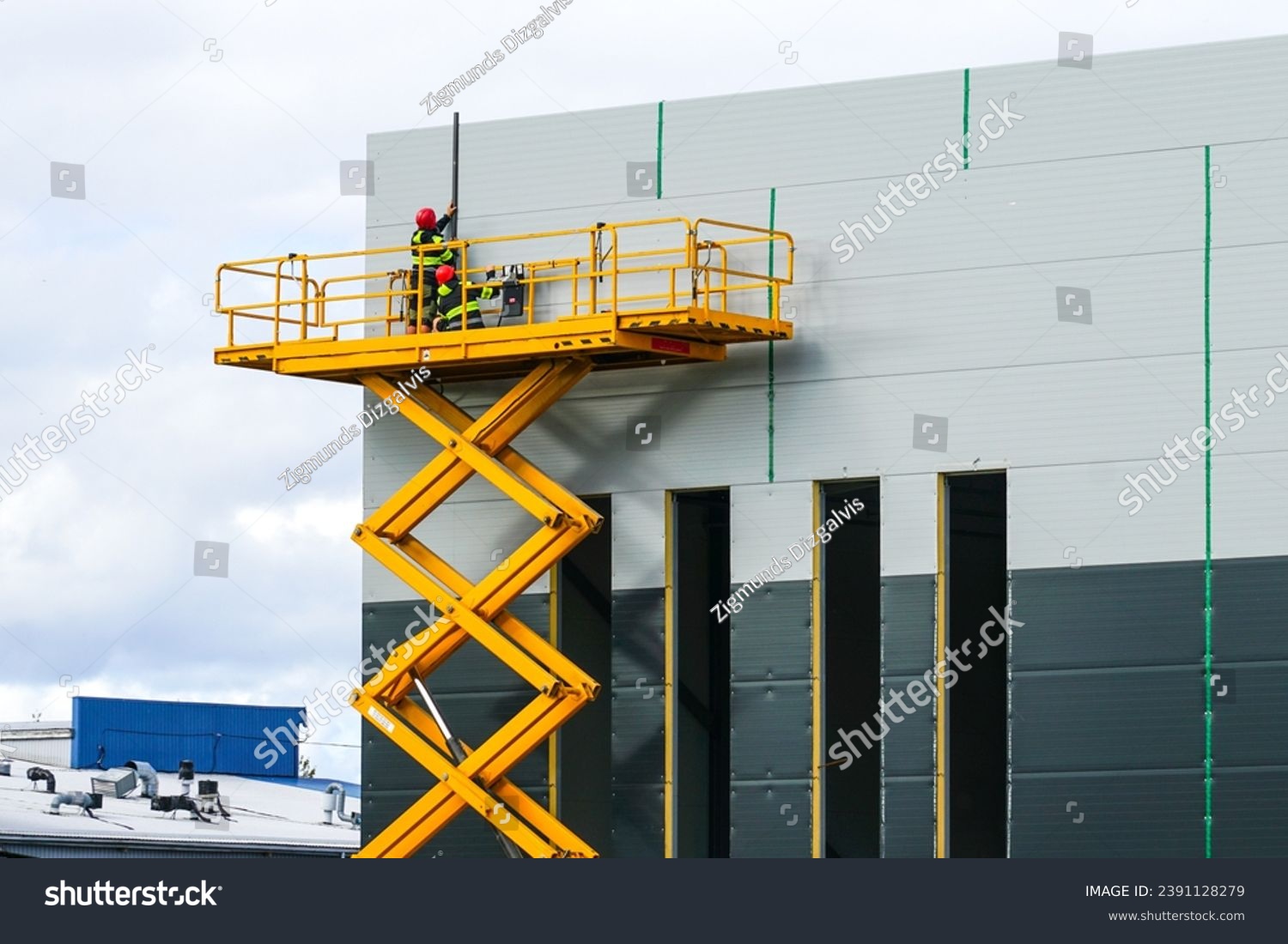 Large elevated aerial scissor lift working platform with workers against grey sandwich panels wall #2391128279