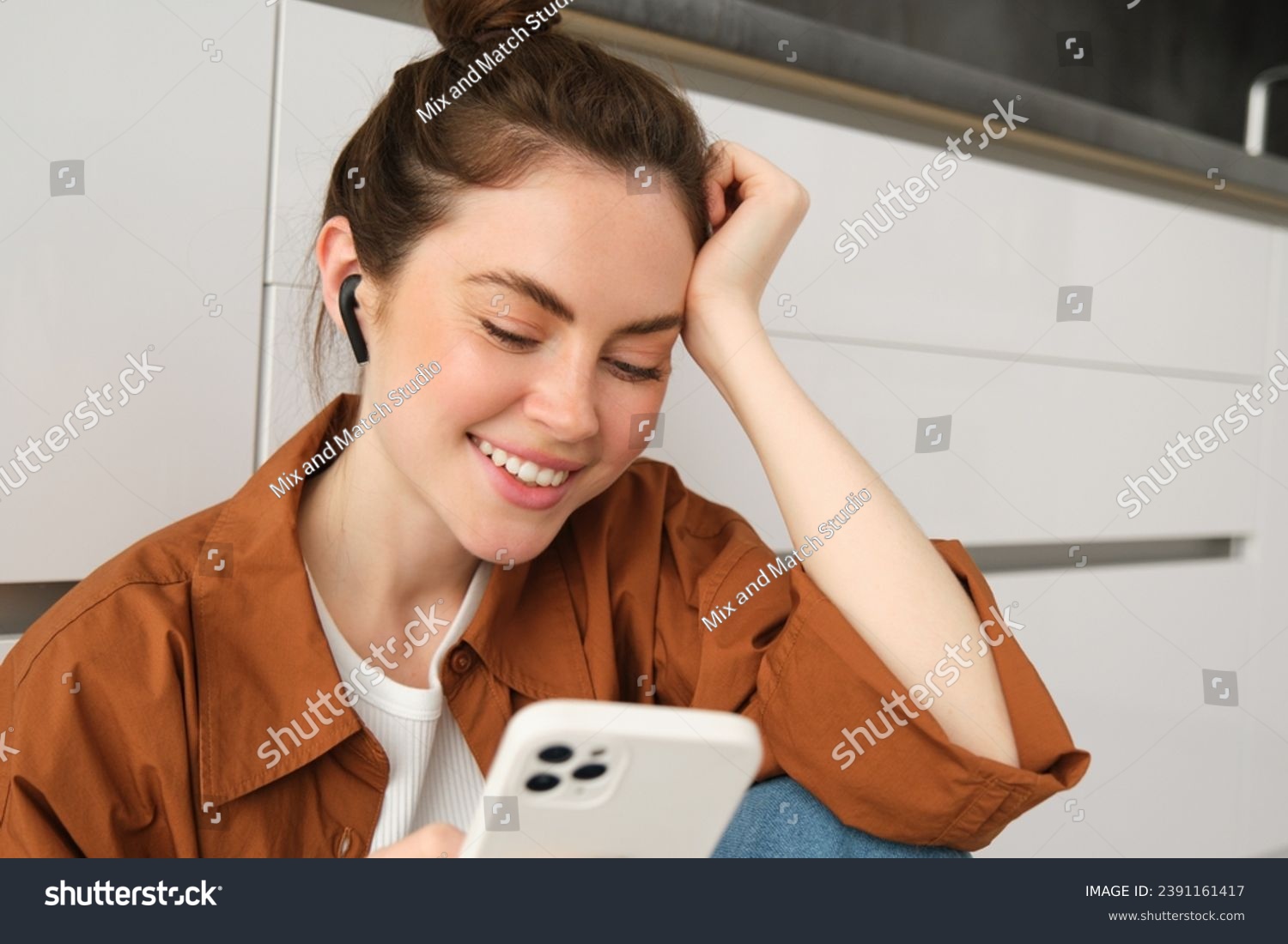 Portrait of happy young beautiful woman, listening music in wireless earphones, using smartphone, watching videos on mobile phone with headphones on. #2391161417