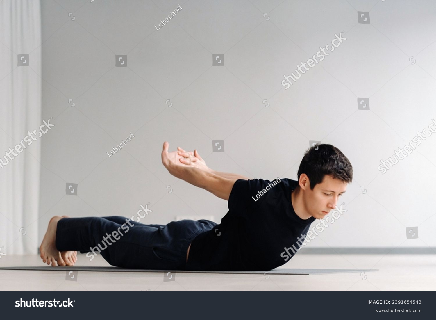 A man in a black T-shirt trains lying down doing stretches in the gym. #2391654543