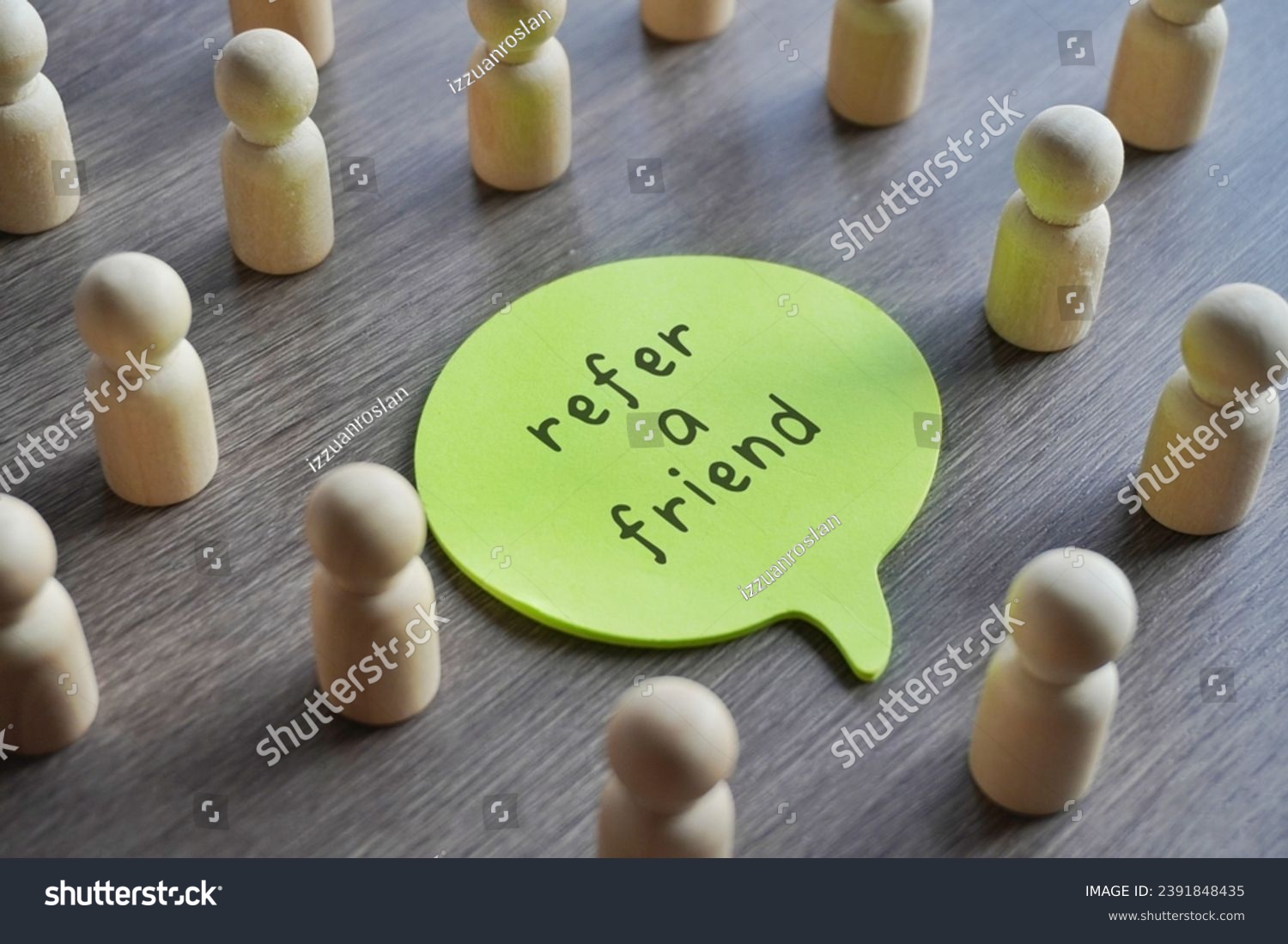 Closeup image of speech bubble with text REFER A FRIEND surrounded by a group of wooden dolls.  #2391848435
