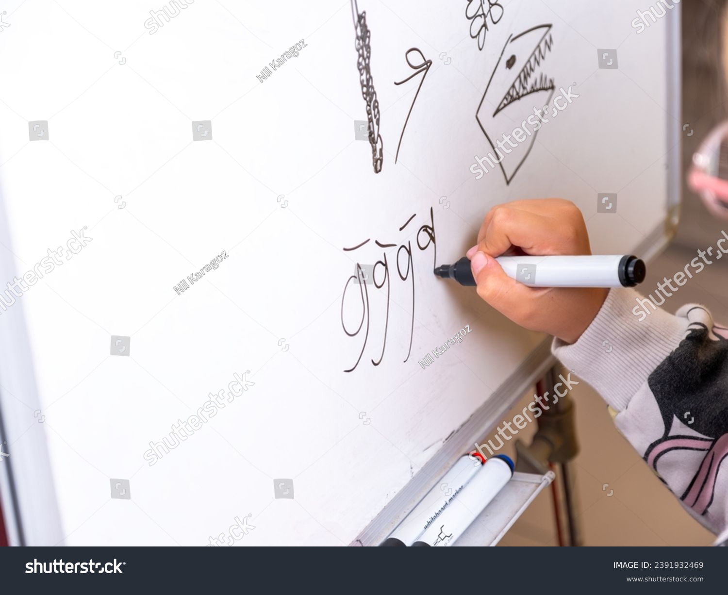 School girl trying to draw the letter g on the whiteboard. School girl learning how to draw. Close-up of school girl's hands drawing on white board.   #2391932469