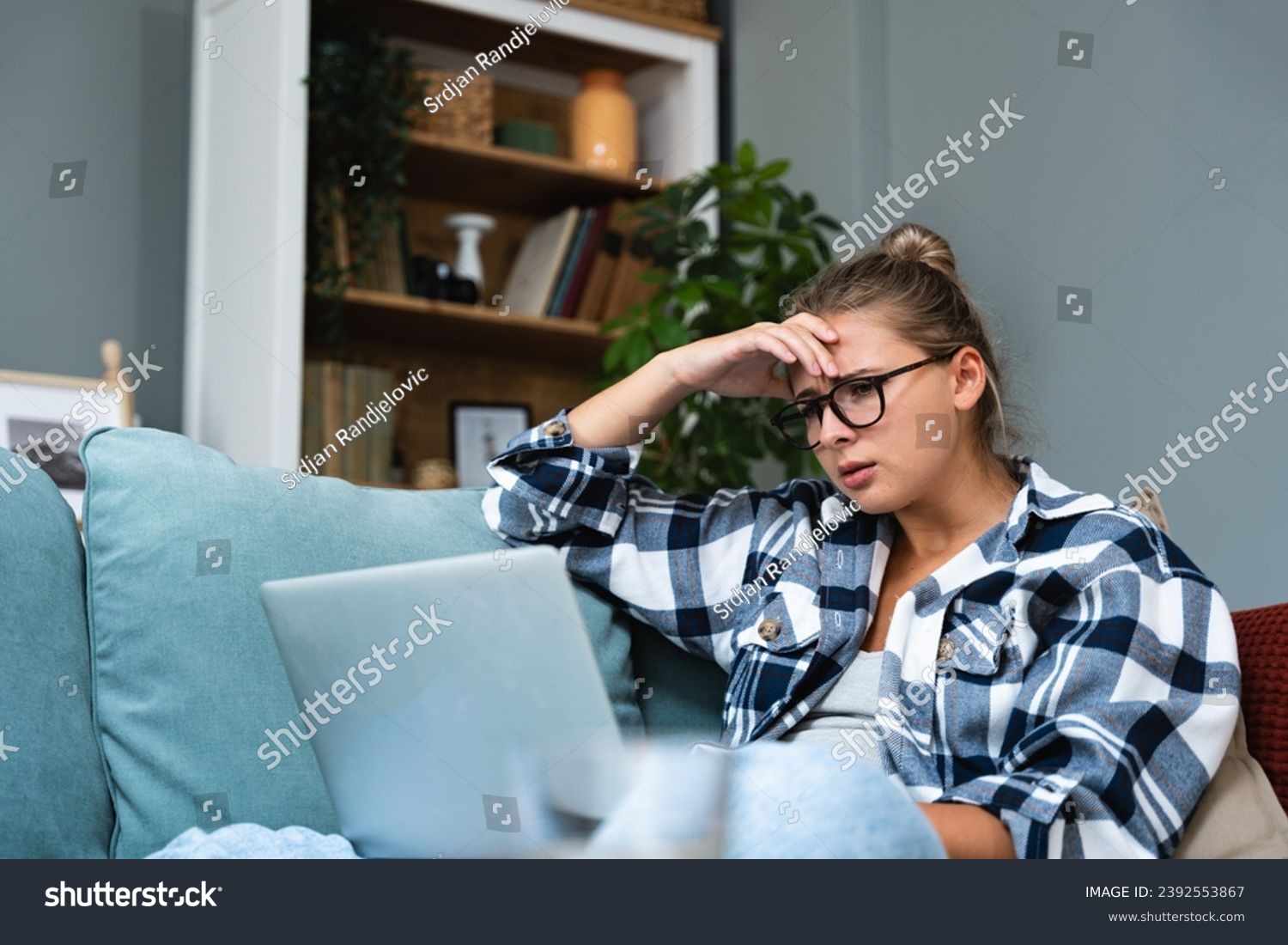 Confused young woman looking on laptop at home feeling bewildered by no connection, reading online news in internet, annoyed teen girl angry with stuck computer problem, scam spam email, system error #2392553867