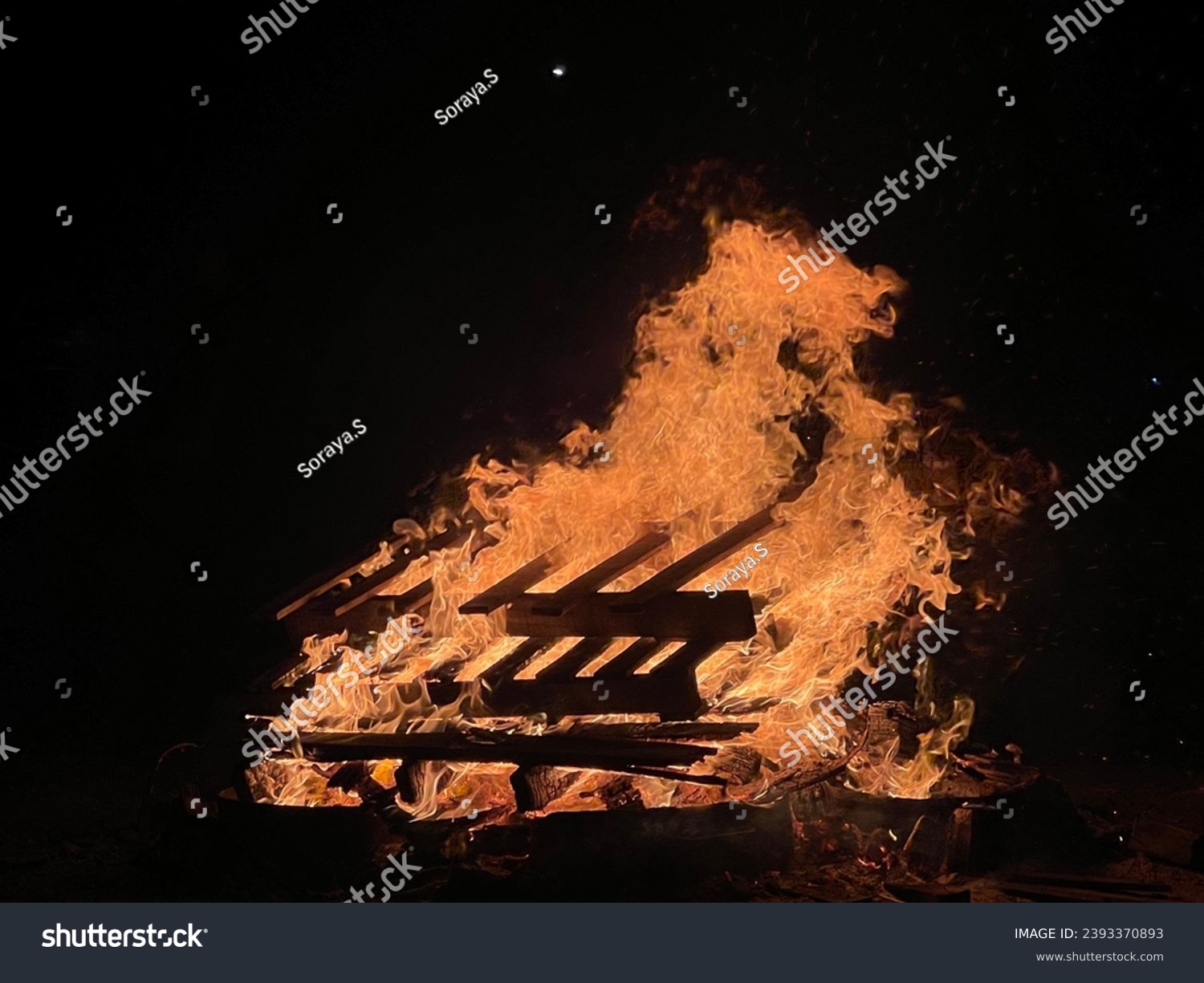 A campfire at campsite that provide light, warmth and heat for cooking. Campfires are a popular feature of camping. Dark background seen with pallete burning #2393370893