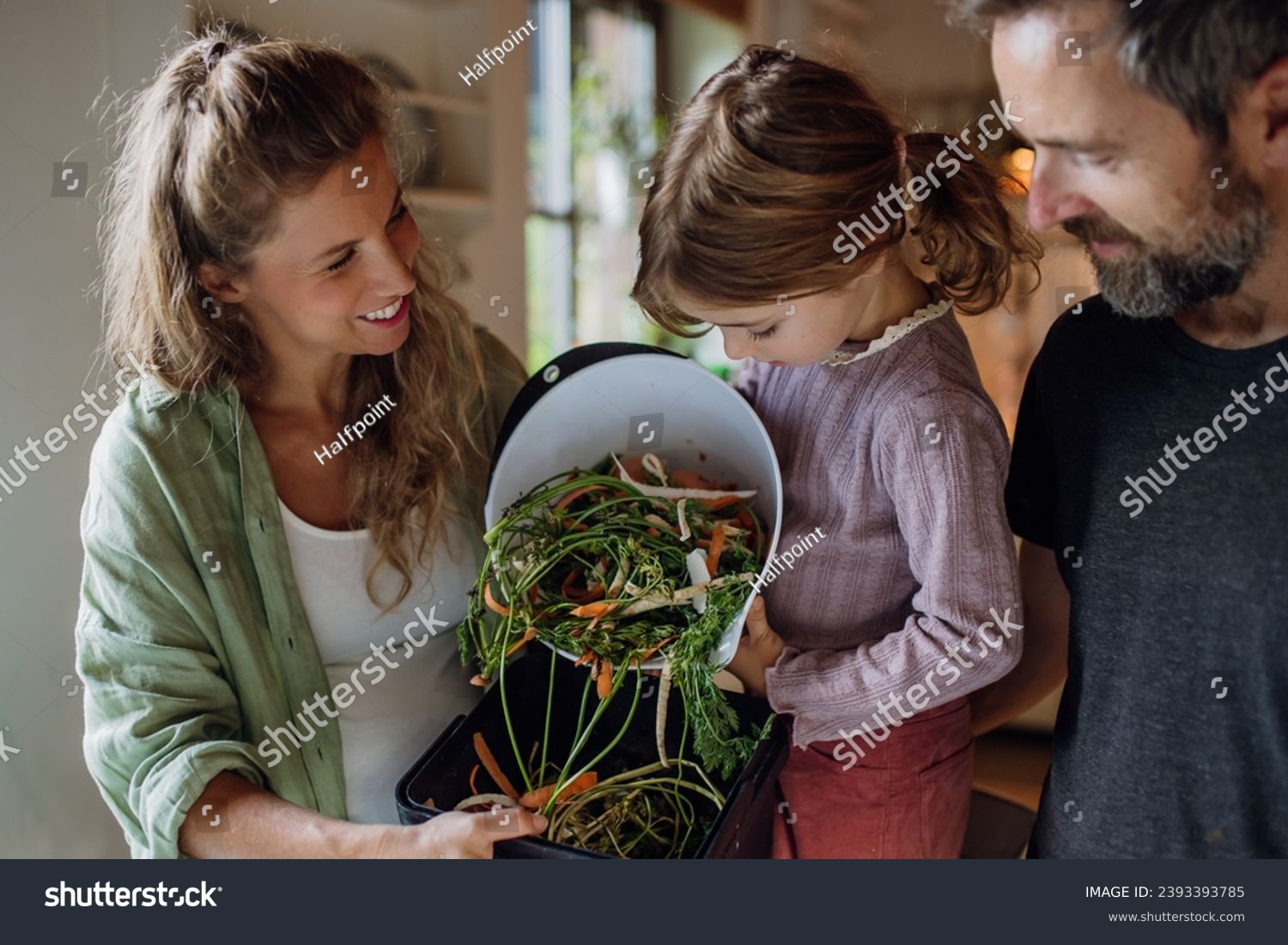 Girl helping parents put kitchen waste, peel and leftover vegetables scraps into kitchen compostable waste. Concept of composting kitchen biodegradable waste. #2393393785